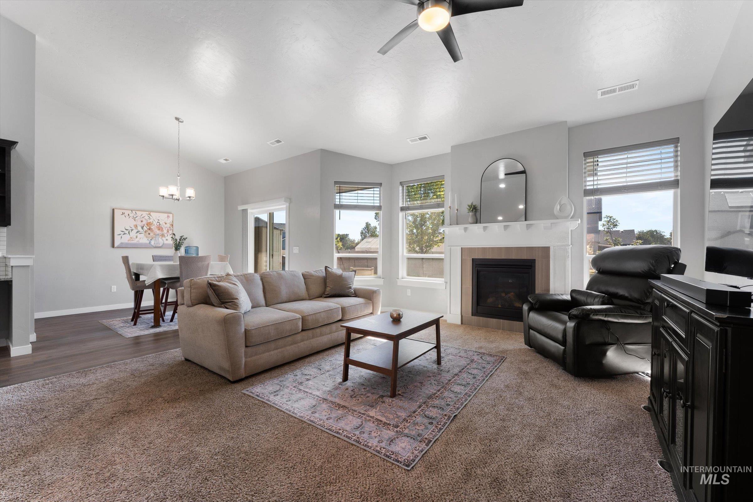 Carpeted living area with a tile fireplace, vaulted ceiling, ceiling fan, and a chandelier