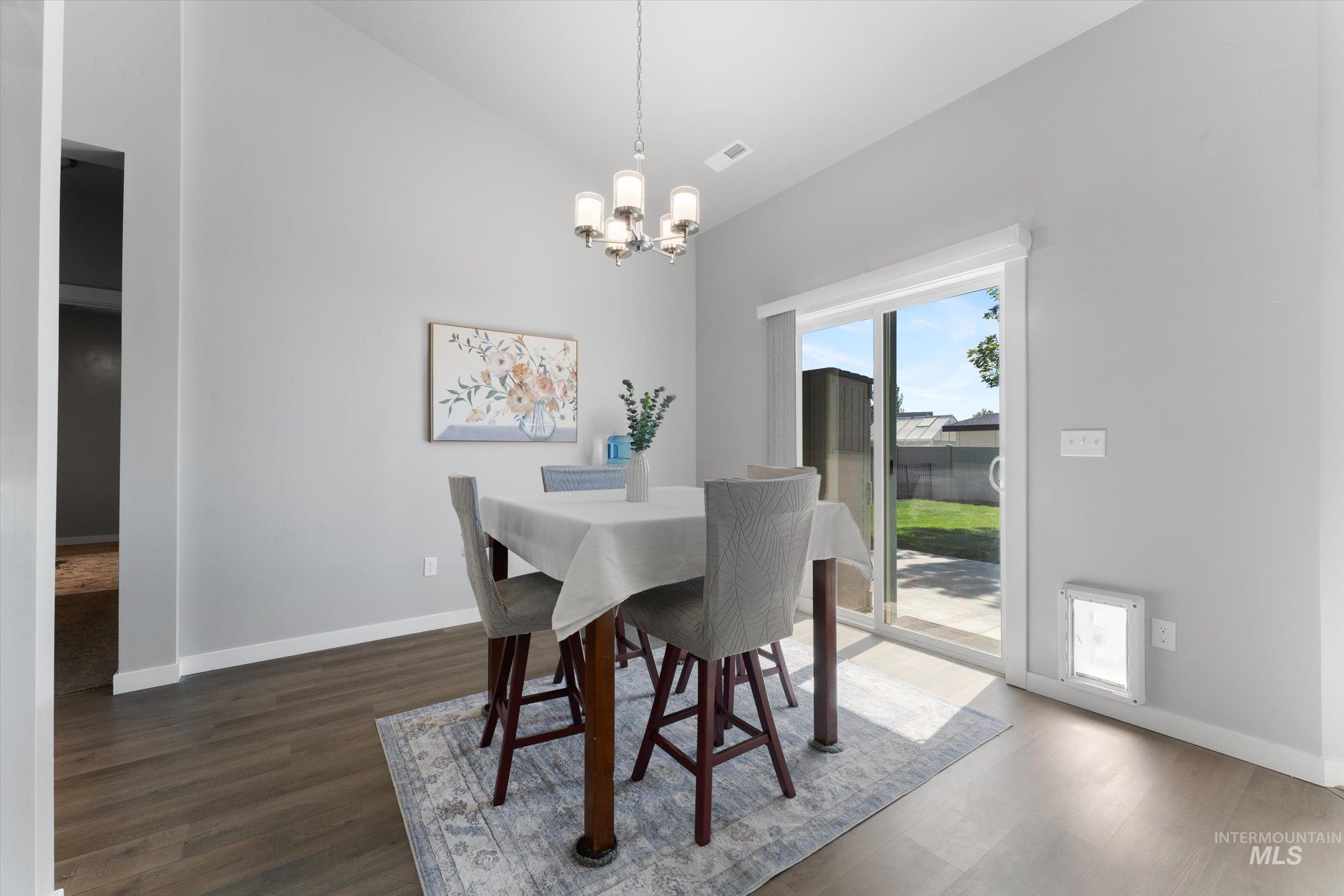 Dining area with dark wood-style flooring, vaulted ceiling, and a chandelier
