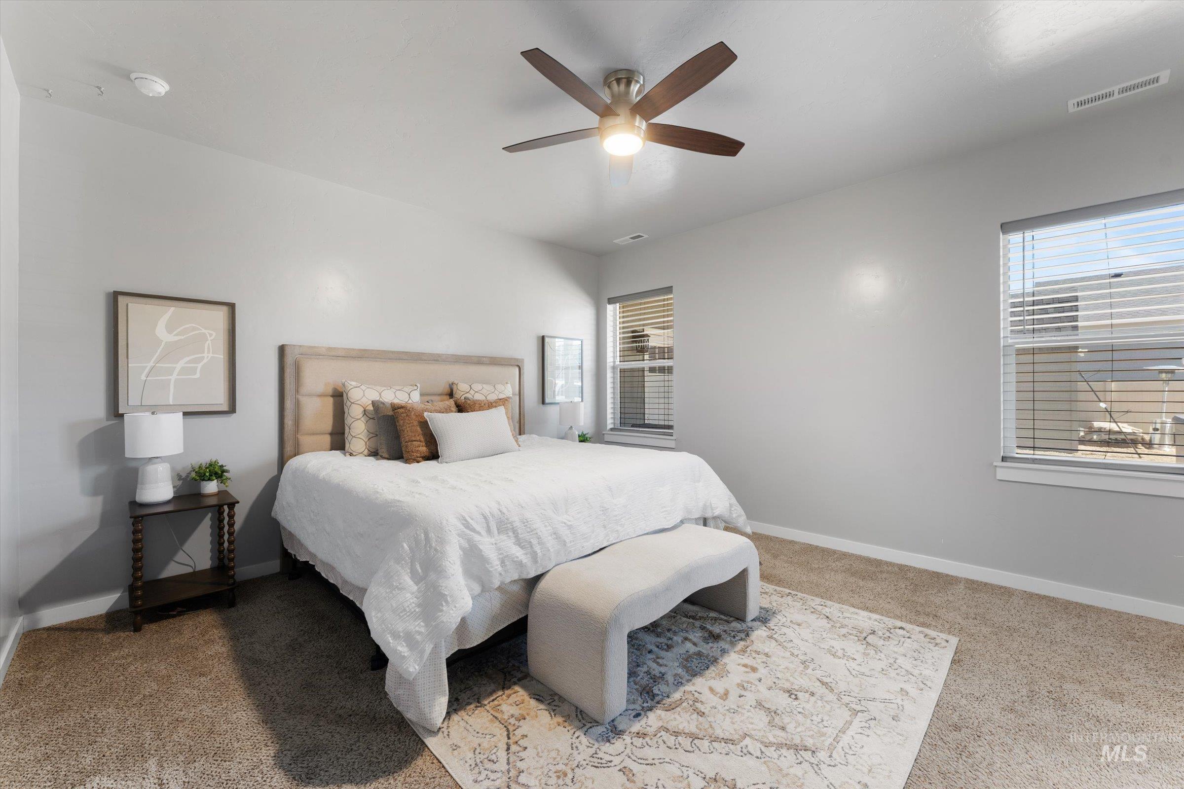 Bedroom with light colored carpet, multiple windows, and ceiling fan