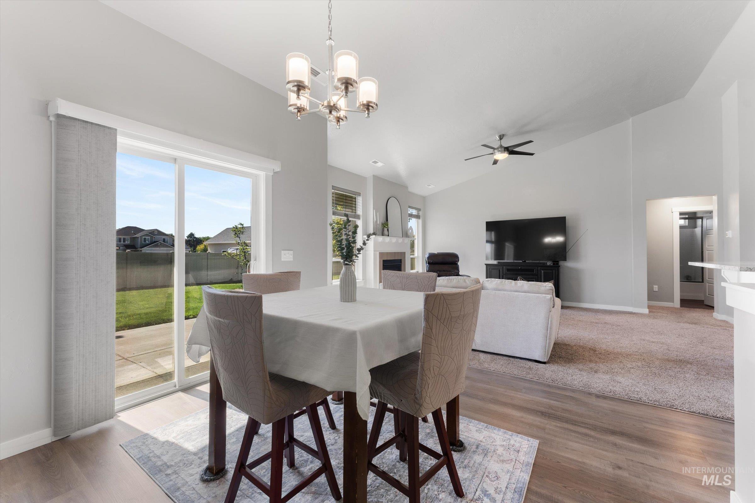Dining space with a fireplace, a chandelier, wood finished floors, a ceiling fan, and high vaulted ceiling