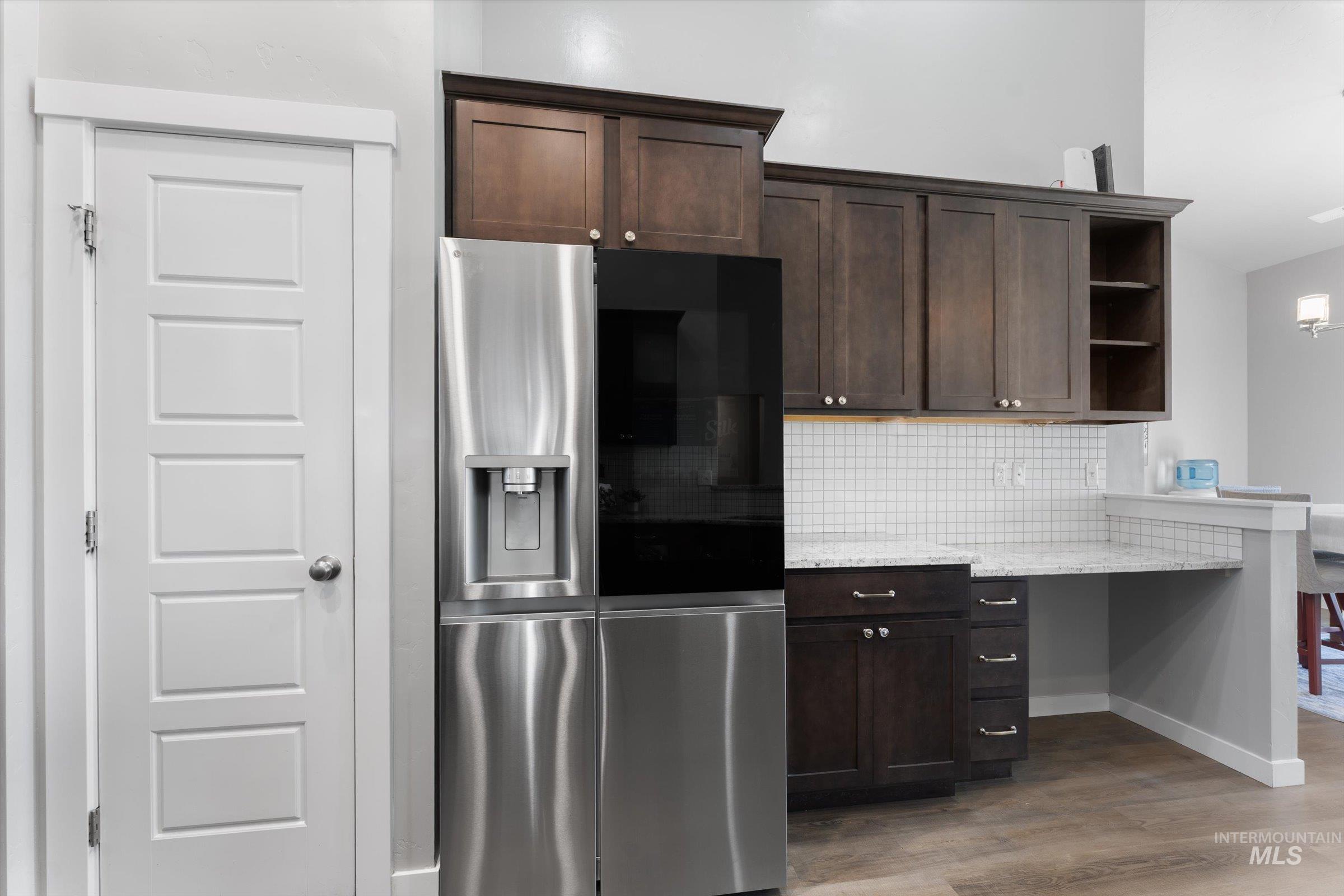 Kitchen featuring stainless steel fridge, dark brown cabinetry, open shelves, backsplash, and light stone counters