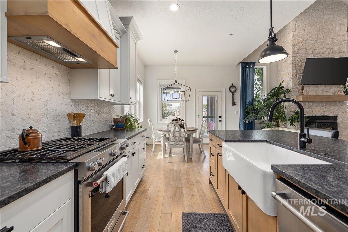 Kitchen featuring appliances with stainless steel finishes, custom exhaust hood, light wood finished floors, hanging light fixtures, and a textured ceiling