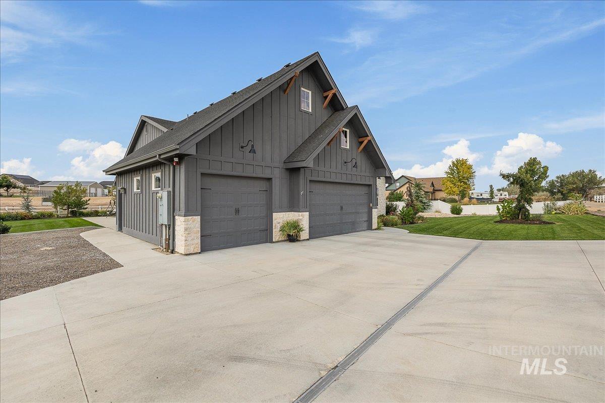 View of property exterior featuring board and batten siding, driveway, a garage, and a yard