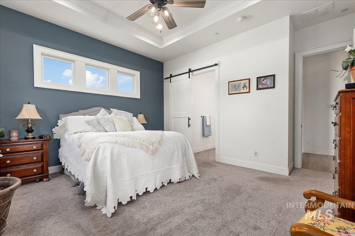 Bedroom with a tray ceiling, a barn door, carpet floors, ceiling fan, and ornamental molding