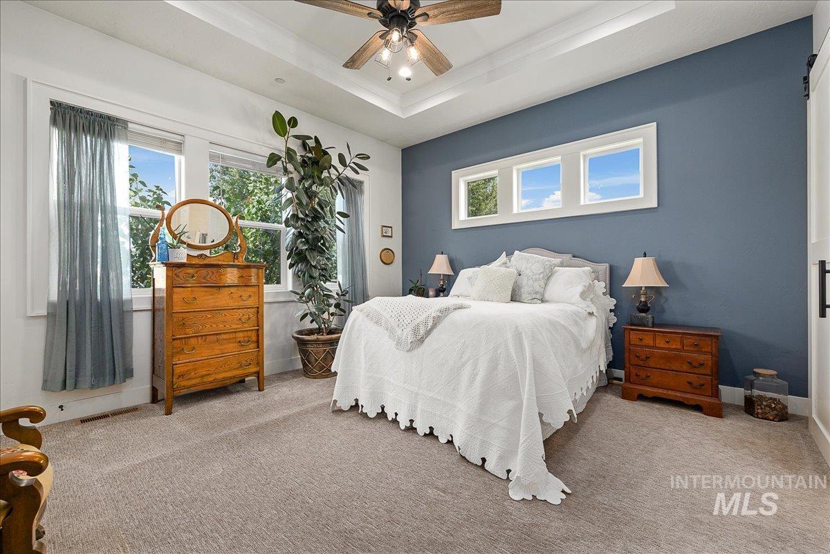 Carpeted bedroom featuring a raised ceiling and ceiling fan