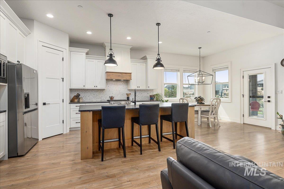 Kitchen featuring decorative backsplash, stainless steel fridge with ice dispenser, pendant lighting, a breakfast bar area, and recessed lighting