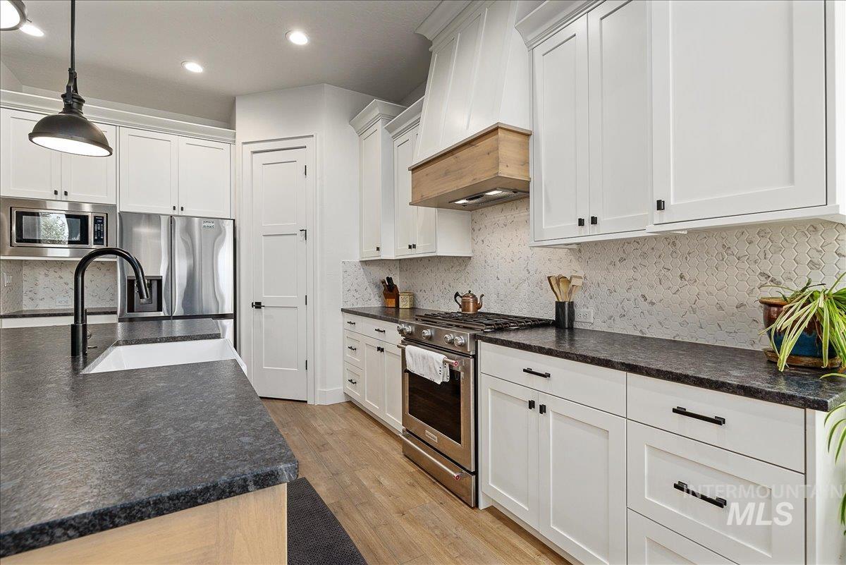 Kitchen featuring appliances with stainless steel finishes, custom exhaust hood, decorative light fixtures, white cabinets, and light wood-style flooring