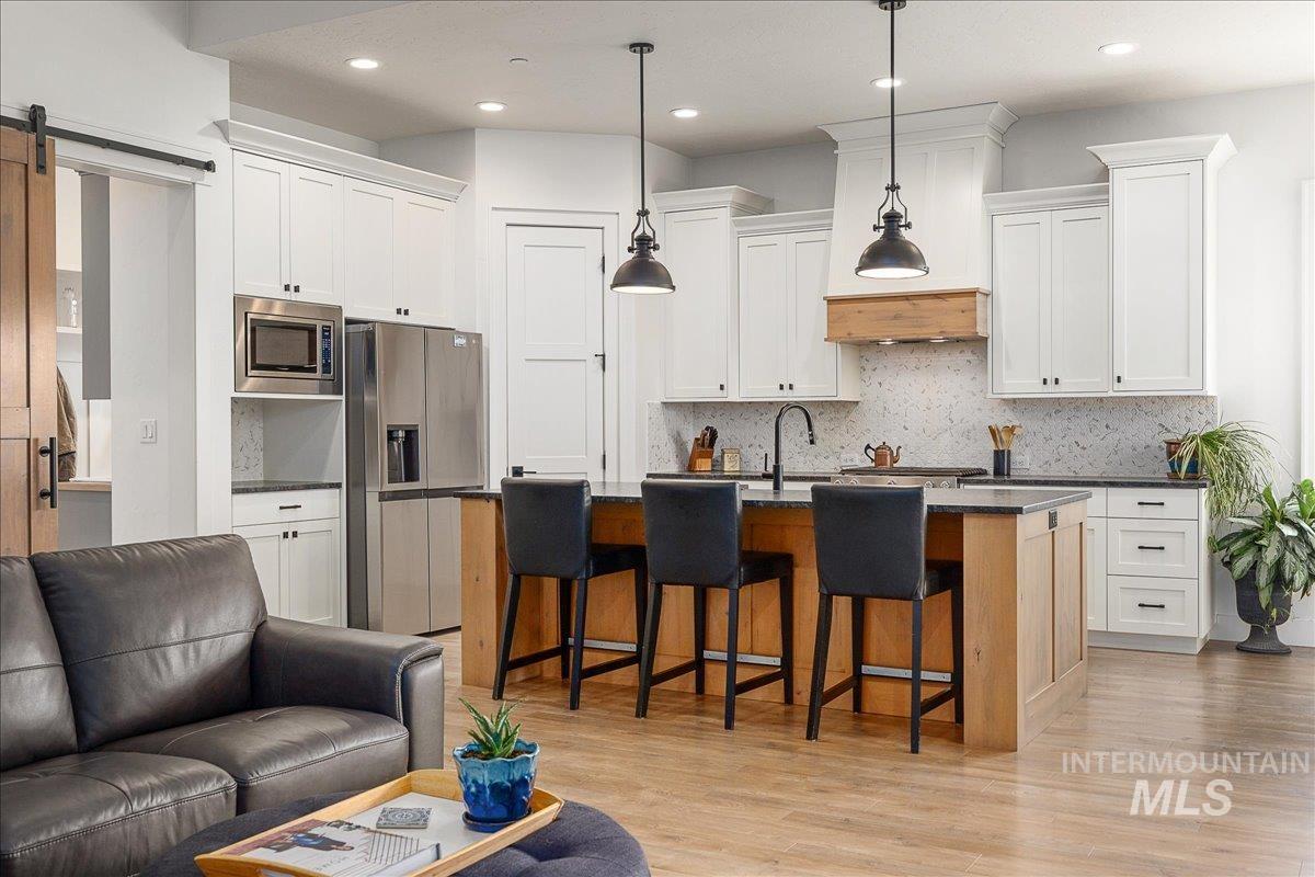 Kitchen with a breakfast bar area, open floor plan, light wood-style flooring, appliances with stainless steel finishes, and backsplash