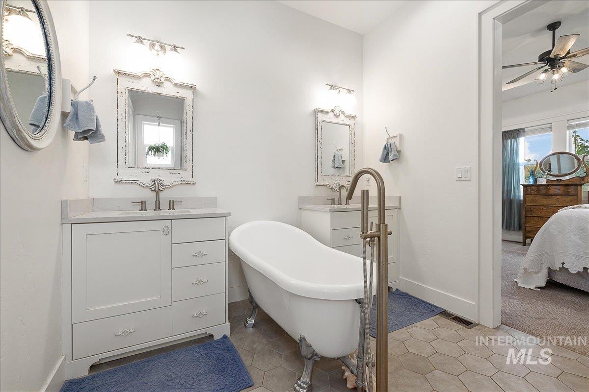 Ensuite bathroom featuring a soaking tub, light tile patterned floors, and two vanities