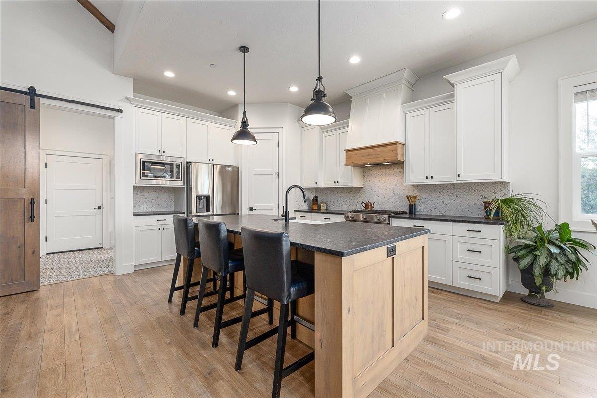 Kitchen with a barn door, a breakfast bar, a center island with sink, stainless steel appliances, and hanging light fixtures