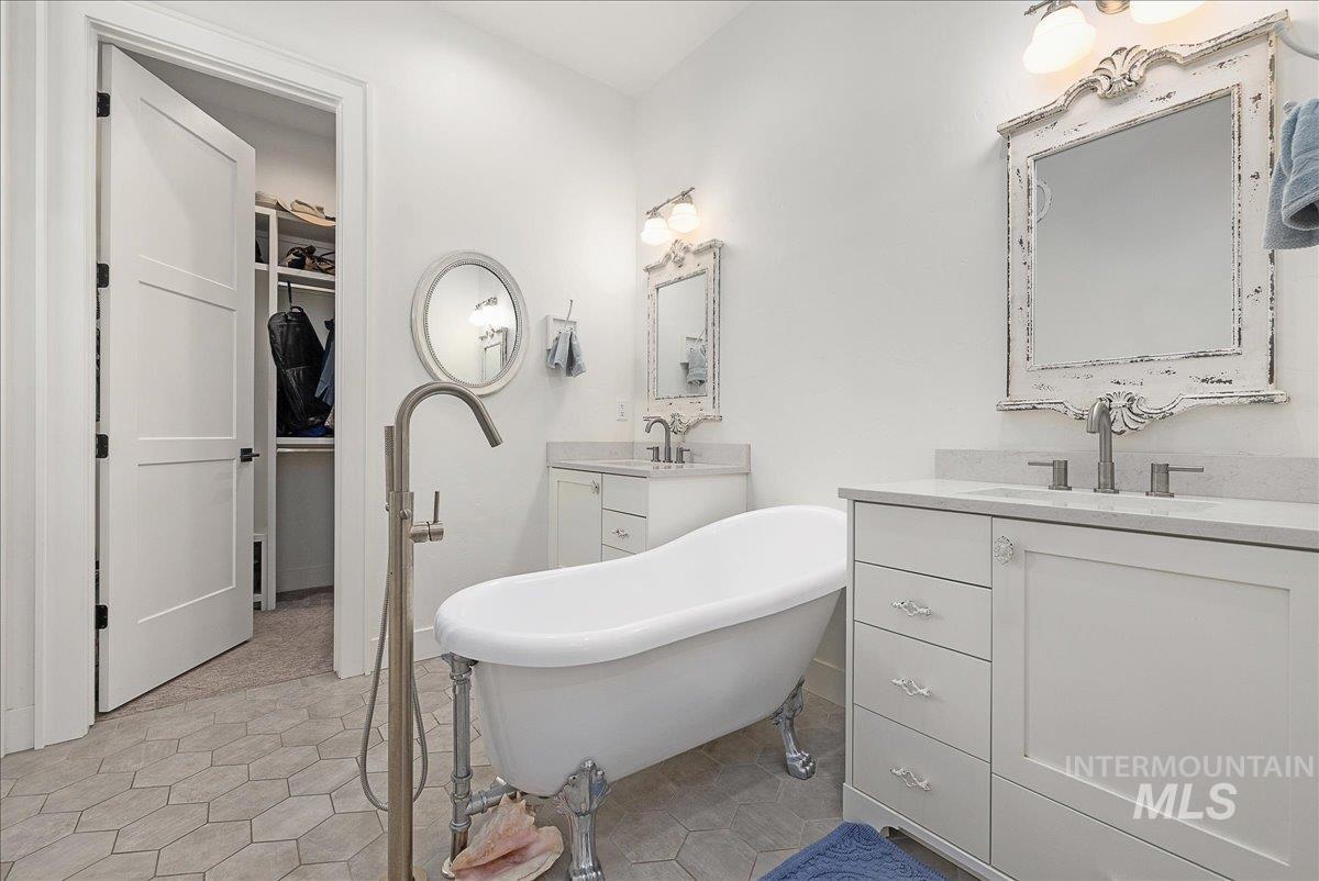 Bathroom featuring a soaking tub, light tile patterned floors, two vanities, and a walk in closet
