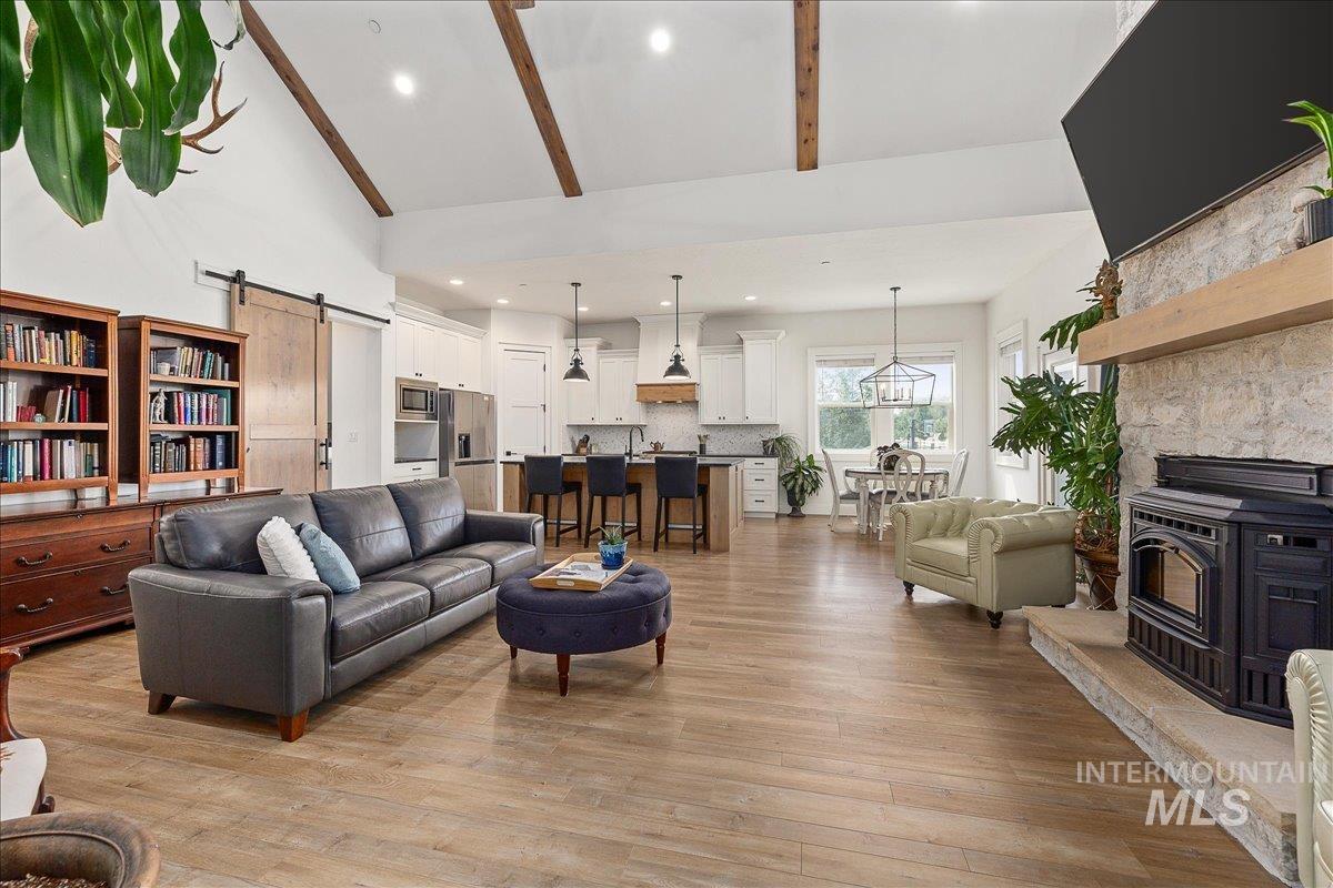 Living room featuring a barn door, a wood stove, beamed ceiling, light wood-style floors, and high vaulted ceiling