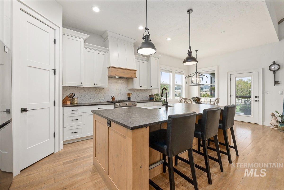 Kitchen with backsplash, a kitchen bar, light wood finished floors, a center island with sink, and recessed lighting