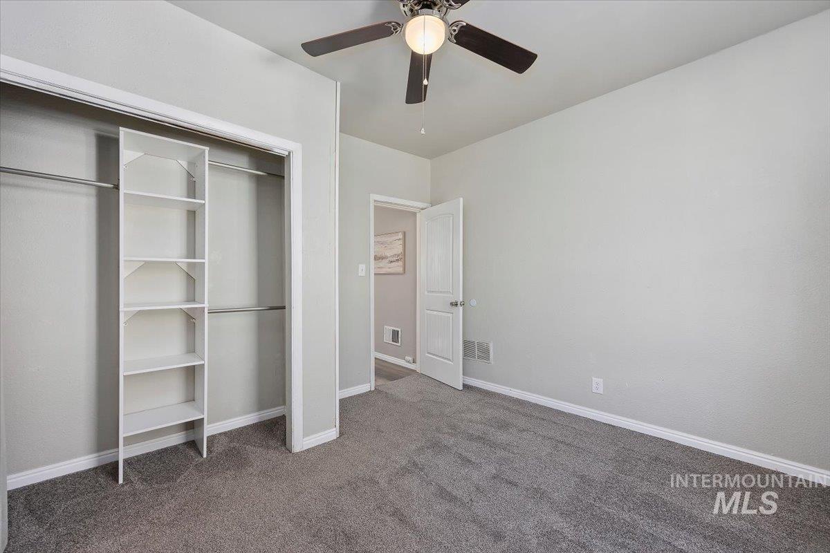 Unfurnished bedroom with dark carpet, a closet, and a ceiling fan
