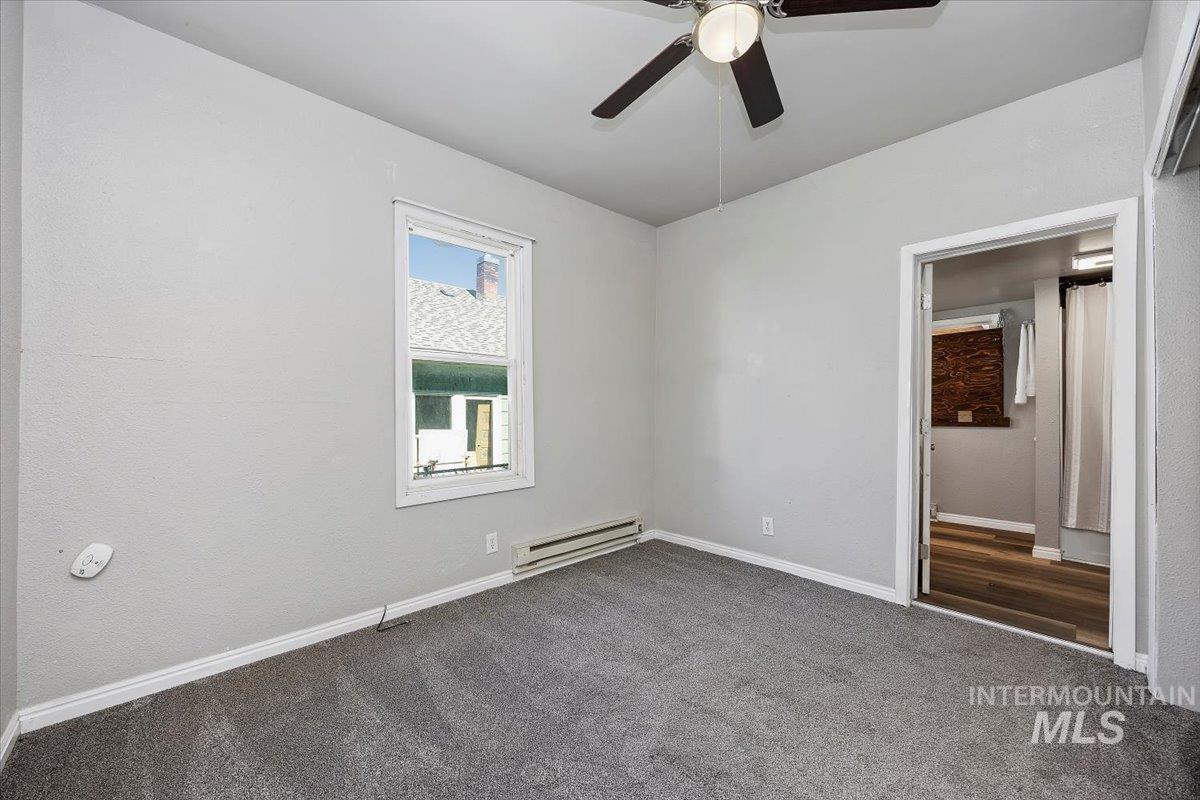 Unfurnished bedroom featuring baseboard heating, dark carpet, a ceiling fan, and ensuite bathroom