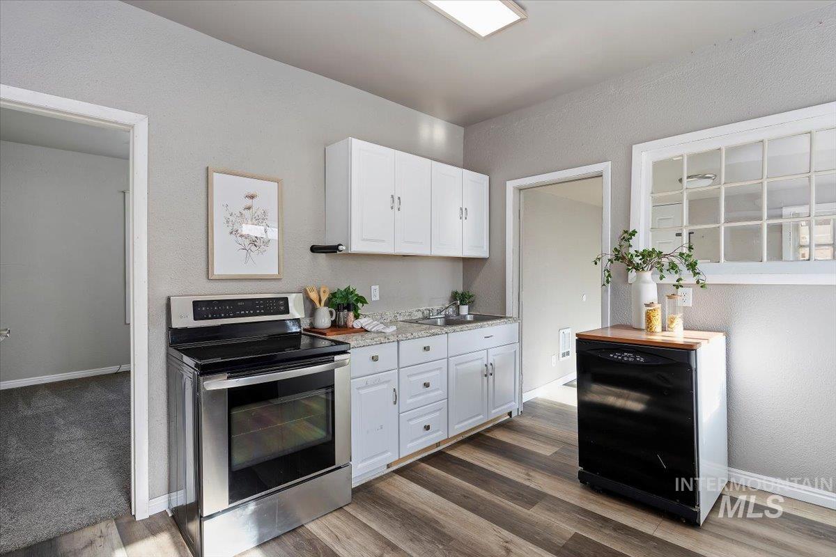 Kitchen featuring electric stove, a textured wall, light countertops, white cabinets, and dark wood-style floors