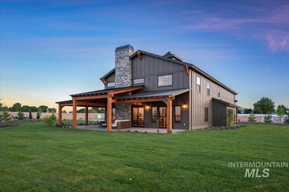 Back of house featuring board and batten siding, a patio area, a chimney, and a lawn