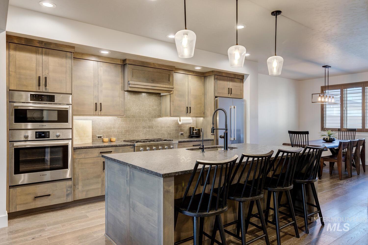 Kitchen featuring decorative light fixtures, dark stone counters, a center island with sink, a kitchen bar, and light wood finished floors