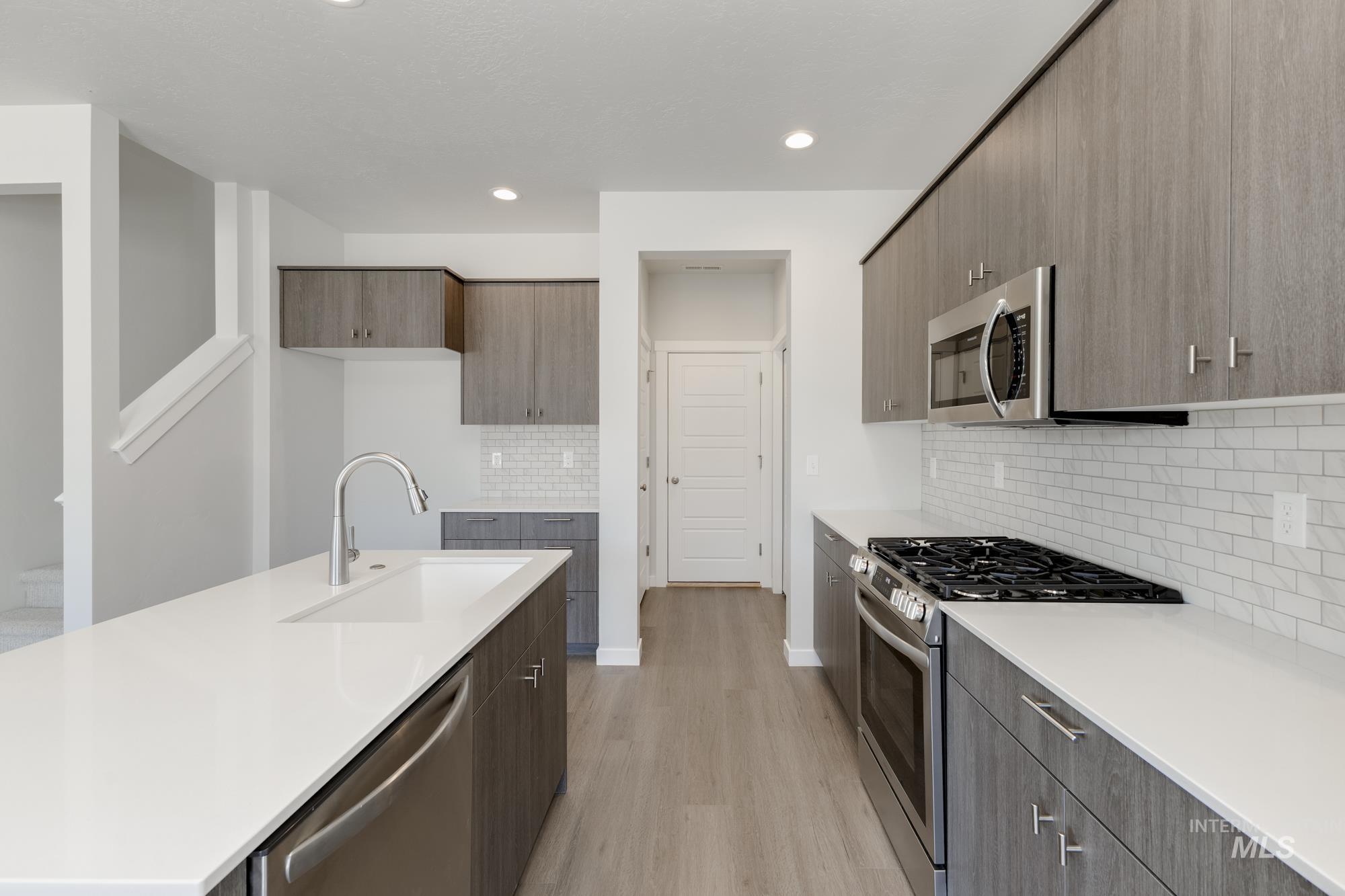 Kitchen with appliances with stainless steel finishes, light wood-type flooring, decorative backsplash, modern cabinets, and light stone counters