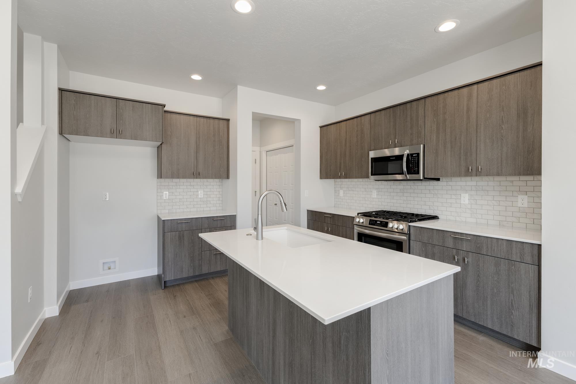 Kitchen with tasteful backsplash, appliances with stainless steel finishes, an island with sink, modern cabinets, and light wood finished floors
