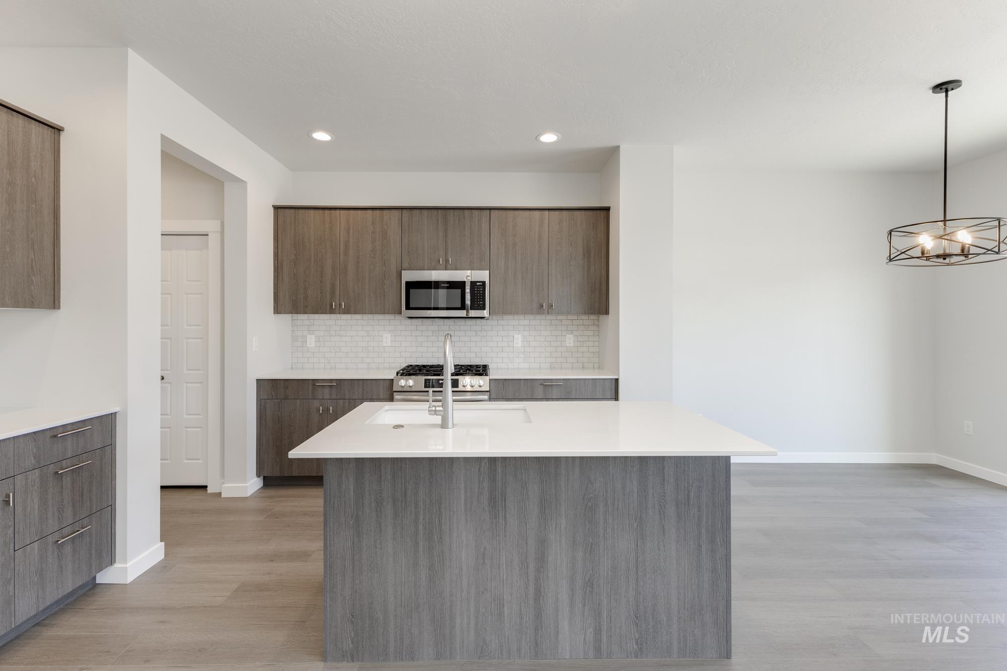 Kitchen with modern cabinets, a center island with sink, appliances with stainless steel finishes, backsplash, and decorative light fixtures