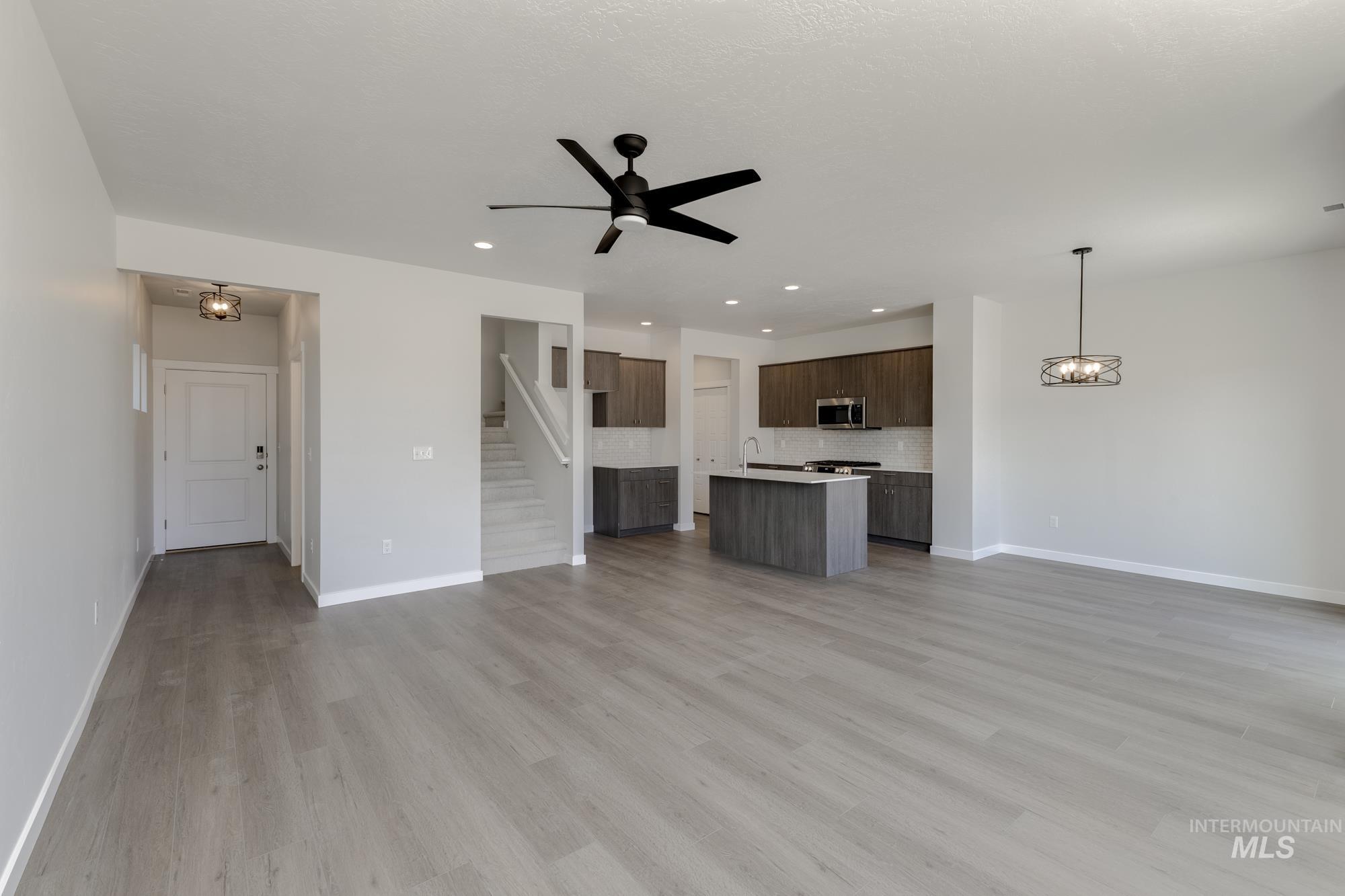 Unfurnished living room with a chandelier, light wood-type flooring, ceiling fan, recessed lighting, and stairway