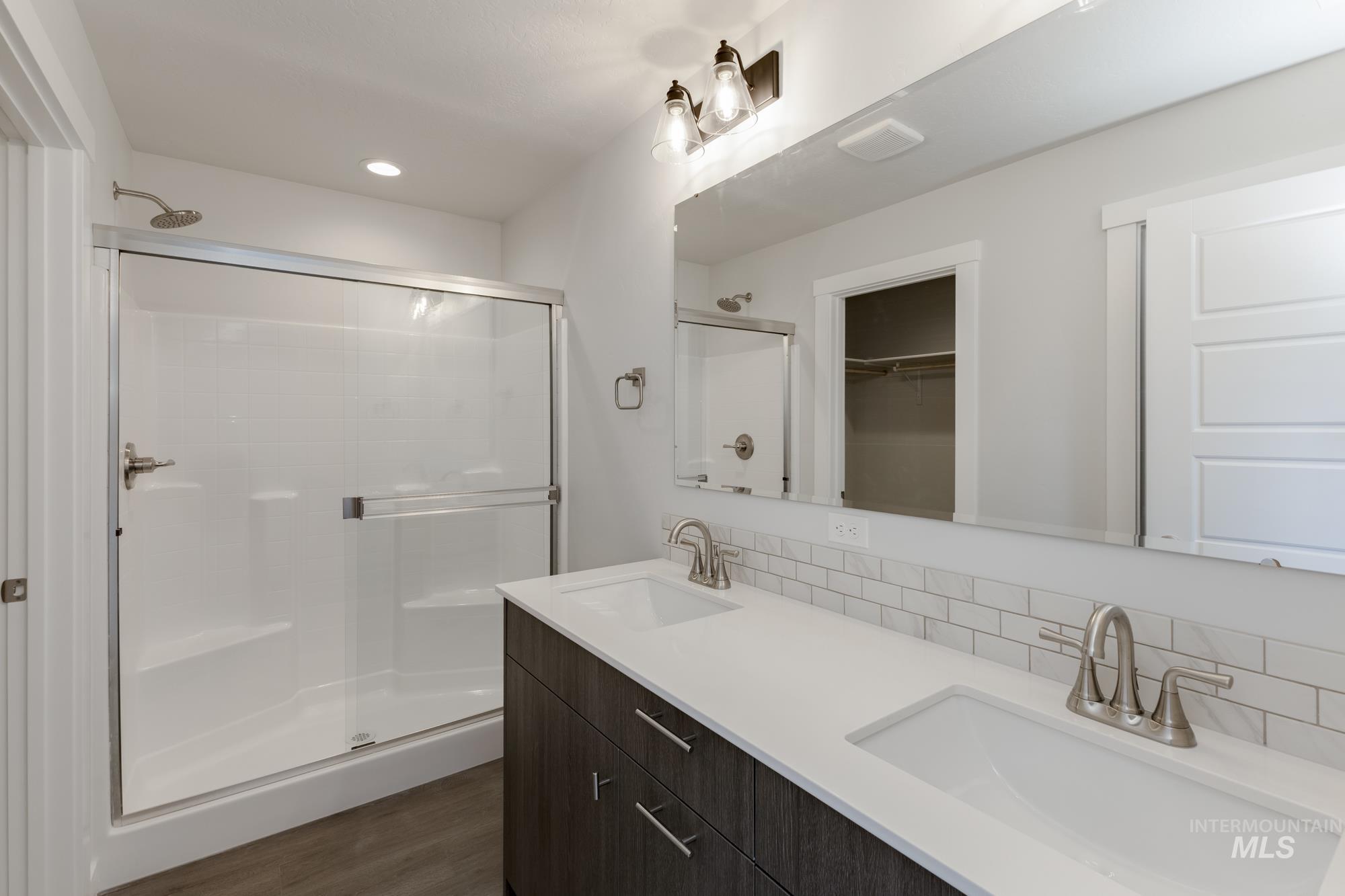 Full bathroom with a shower stall, a spacious closet, dark wood-style flooring, recessed lighting, and double vanity