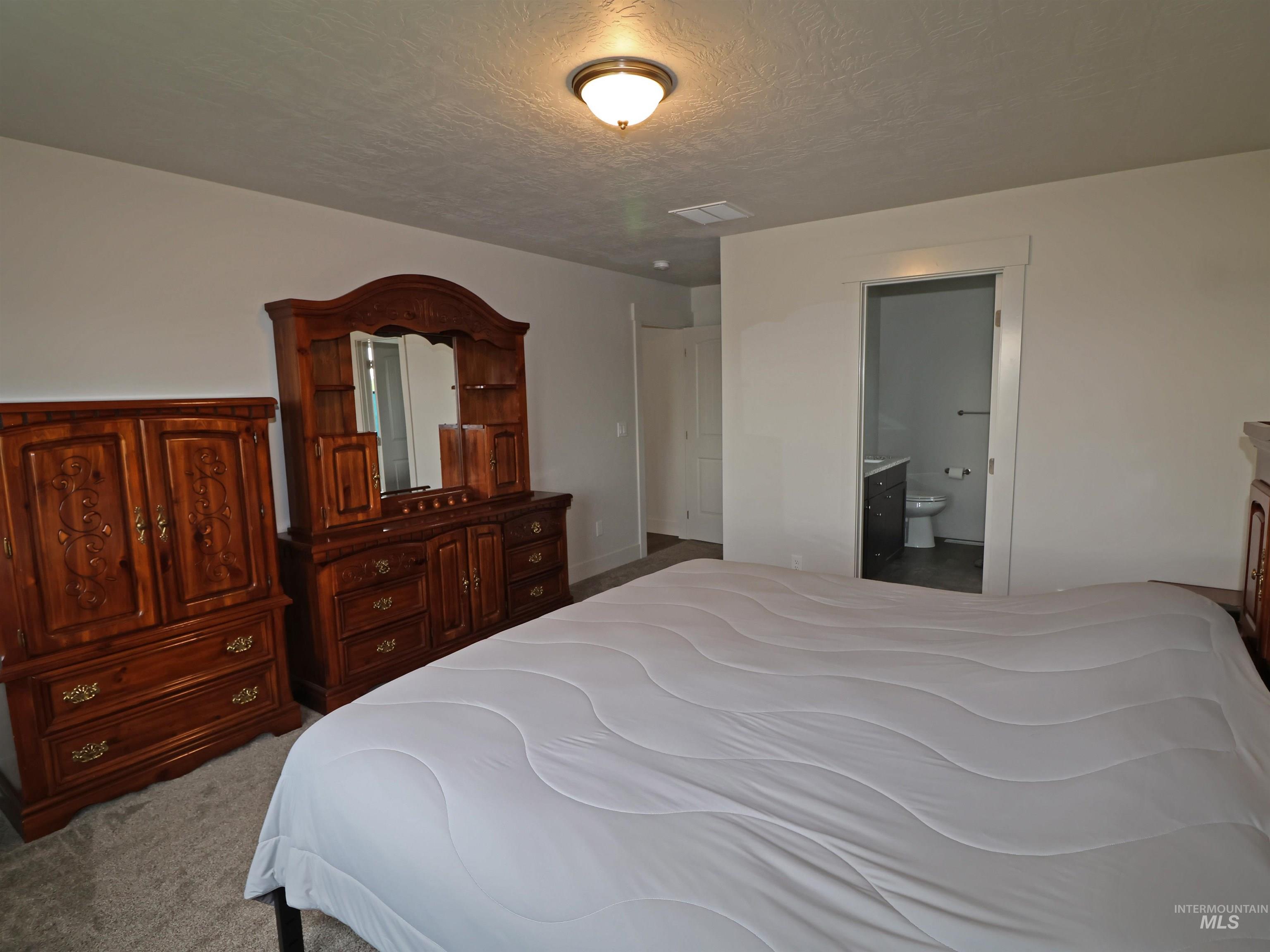 Bedroom with carpet floors, a textured ceiling, and ensuite bath