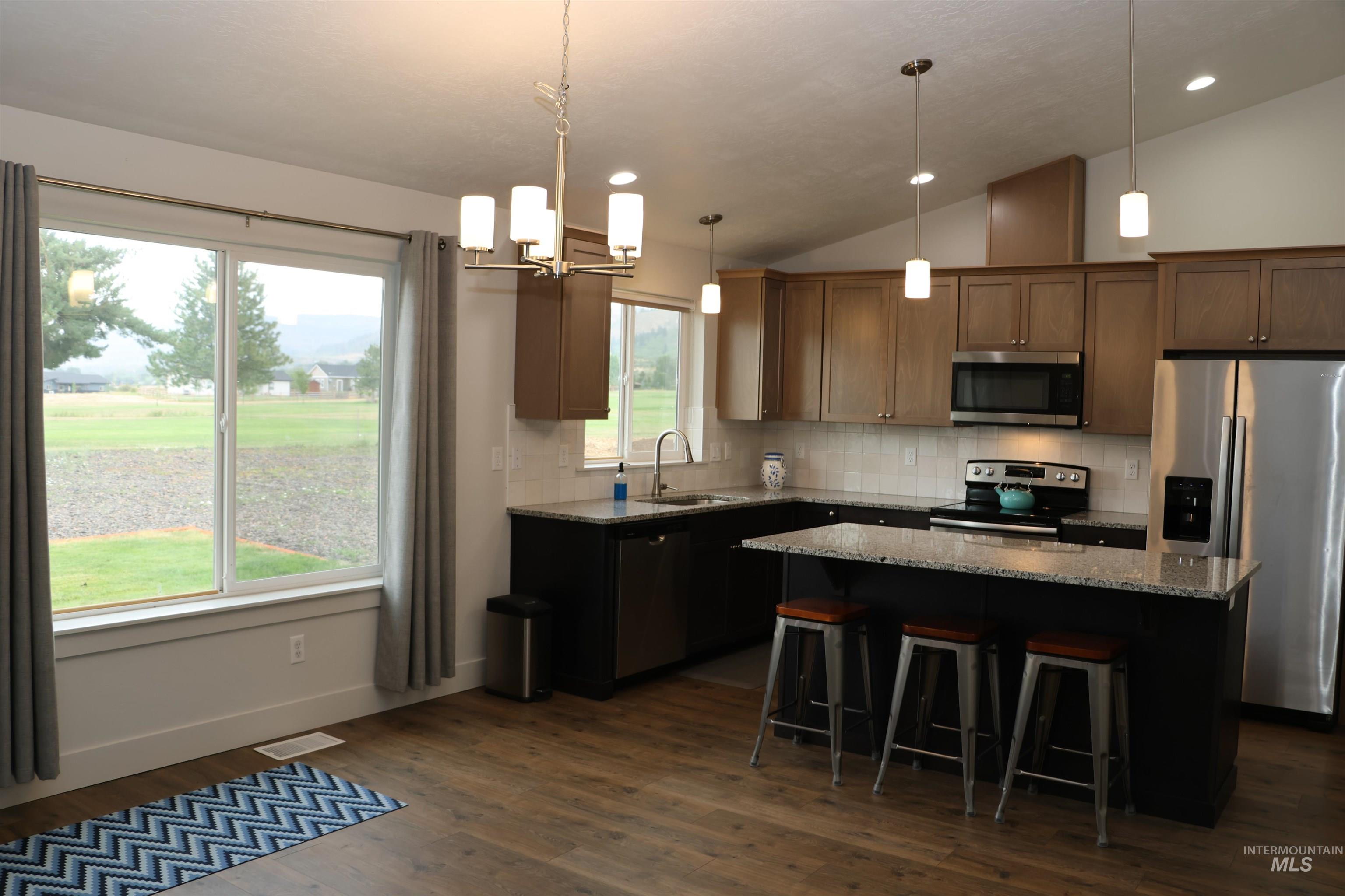 Kitchen featuring lofted ceiling, stainless steel appliances, a kitchen island, dark wood-type flooring, and light stone countertops