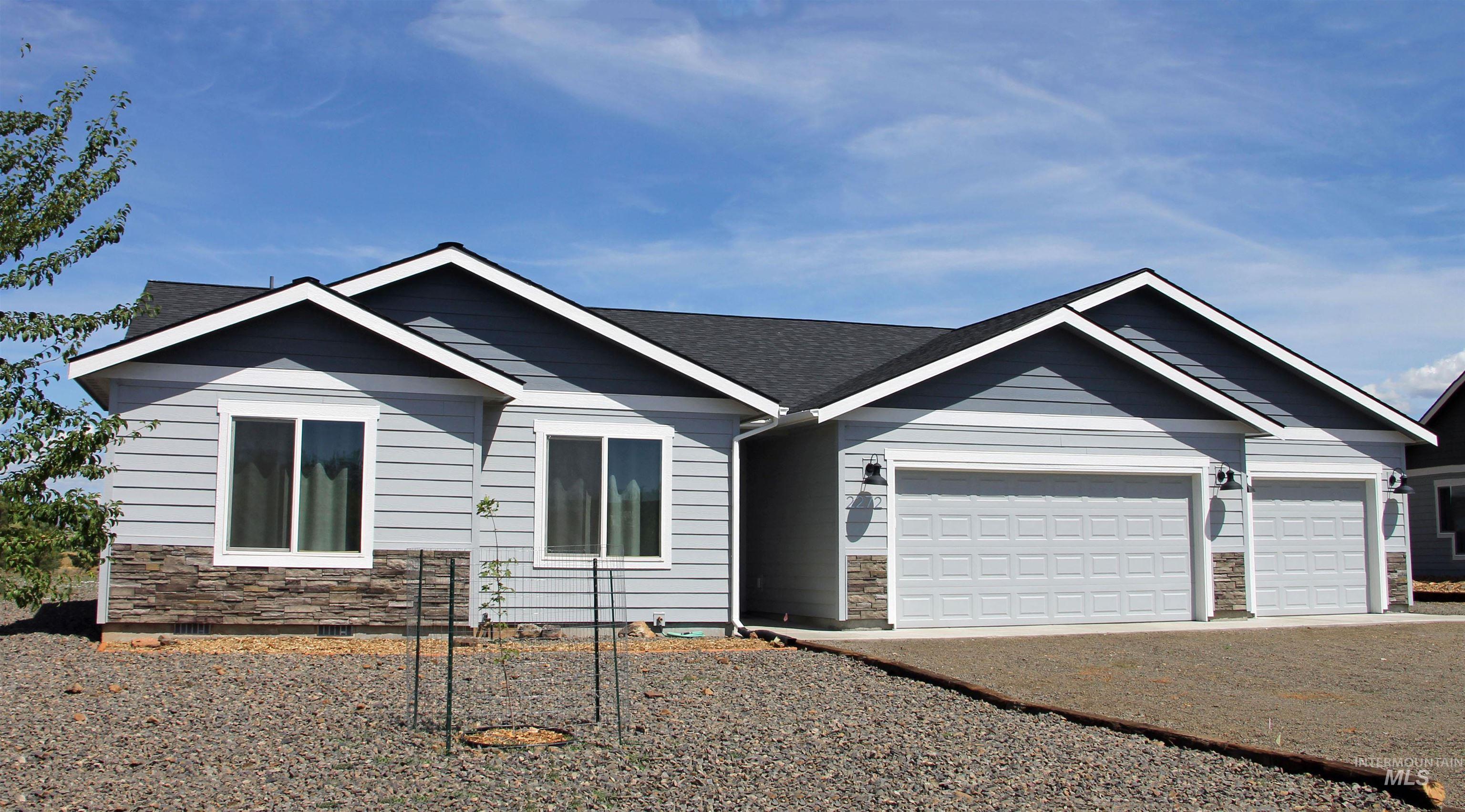 Single story home with stone siding, a garage, and gravel driveway