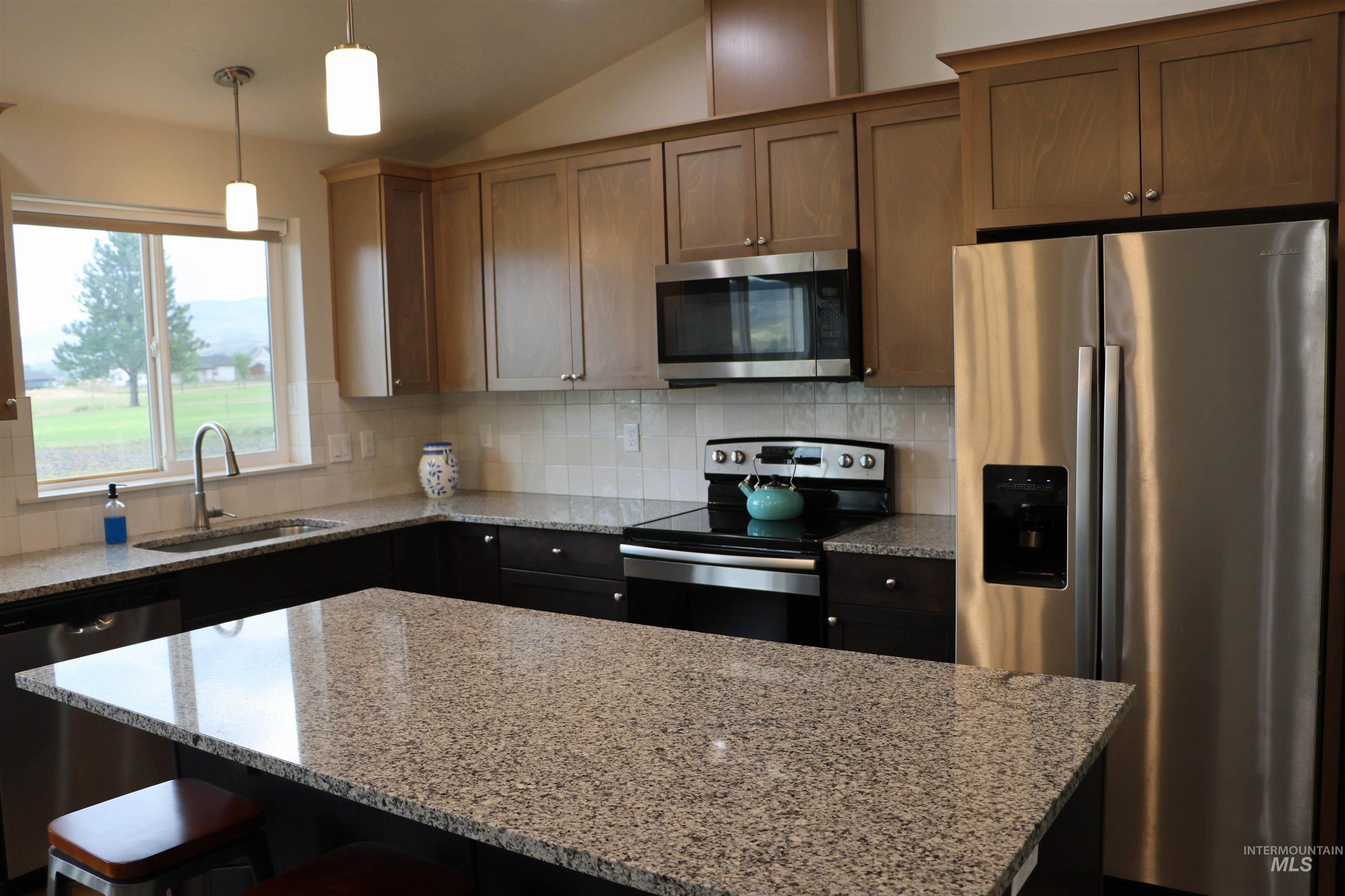 Kitchen featuring stainless steel appliances, lofted ceiling, light stone counters, a kitchen island, and a kitchen bar