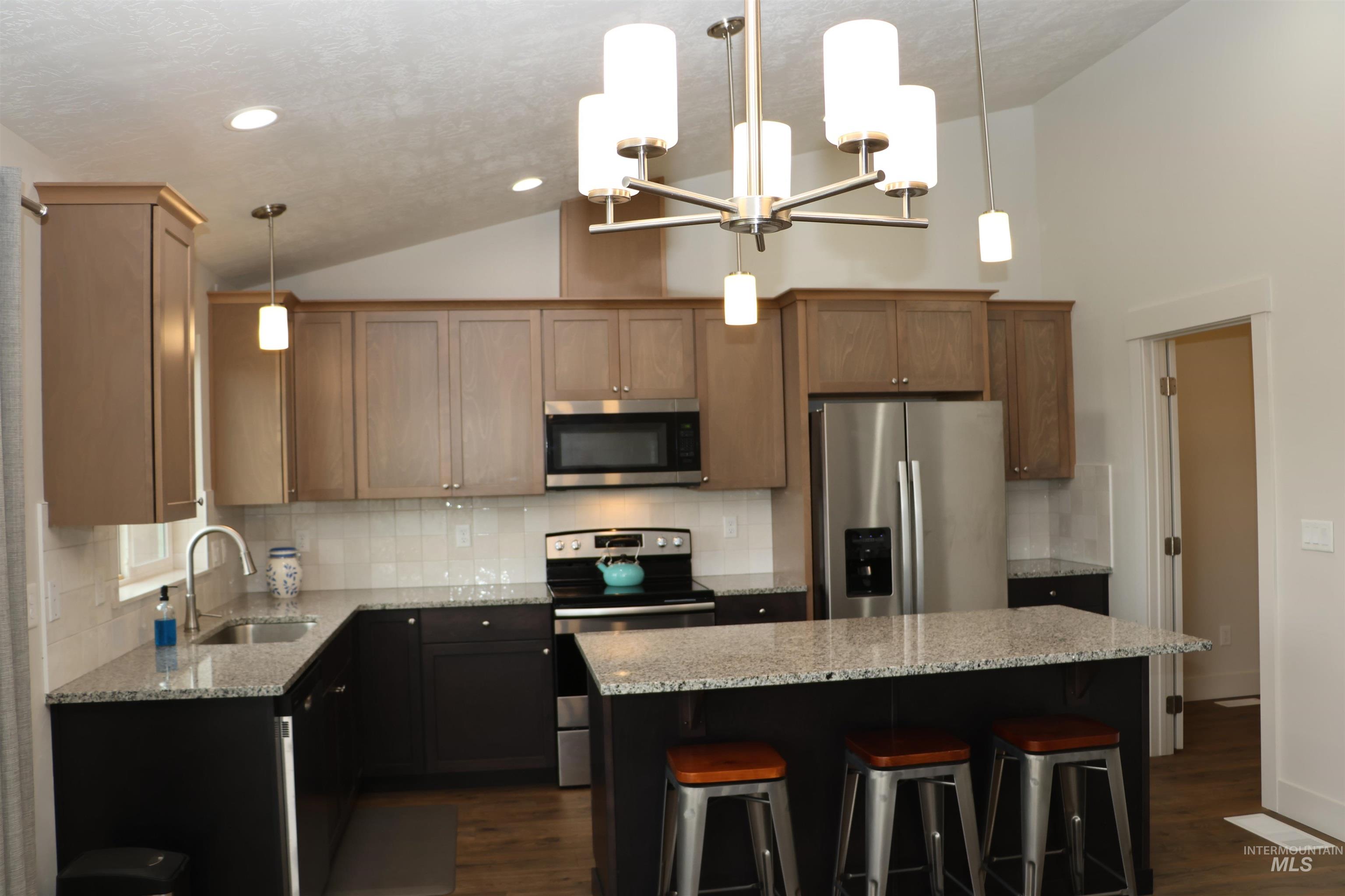 Kitchen featuring stainless steel appliances, dark wood-style flooring, a kitchen island, light stone counters, and decorative backsplash