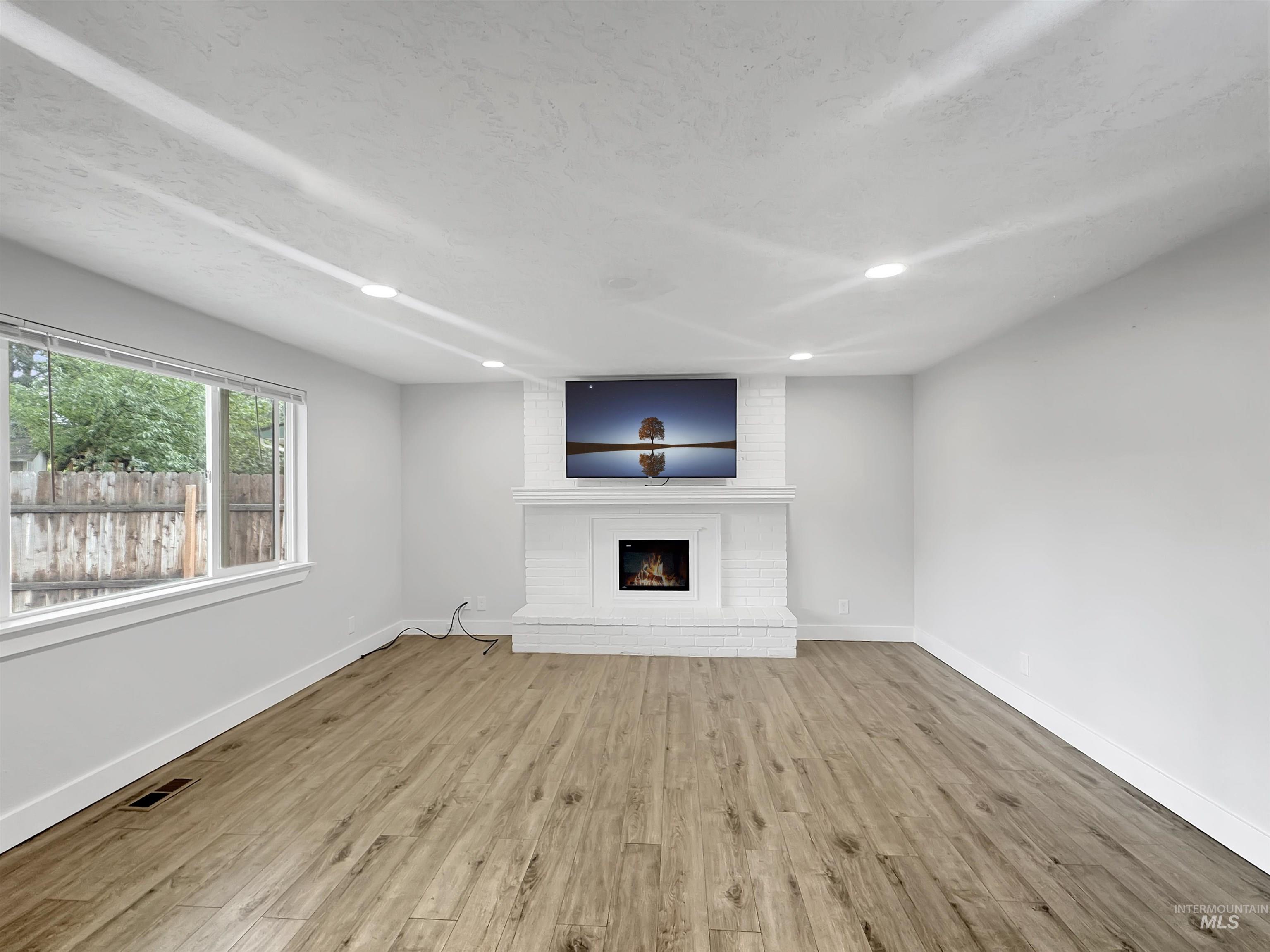 Spacious living area featuring wood-finish flooring, a white brick fireplace with mantel, and recessed ceiling lighting