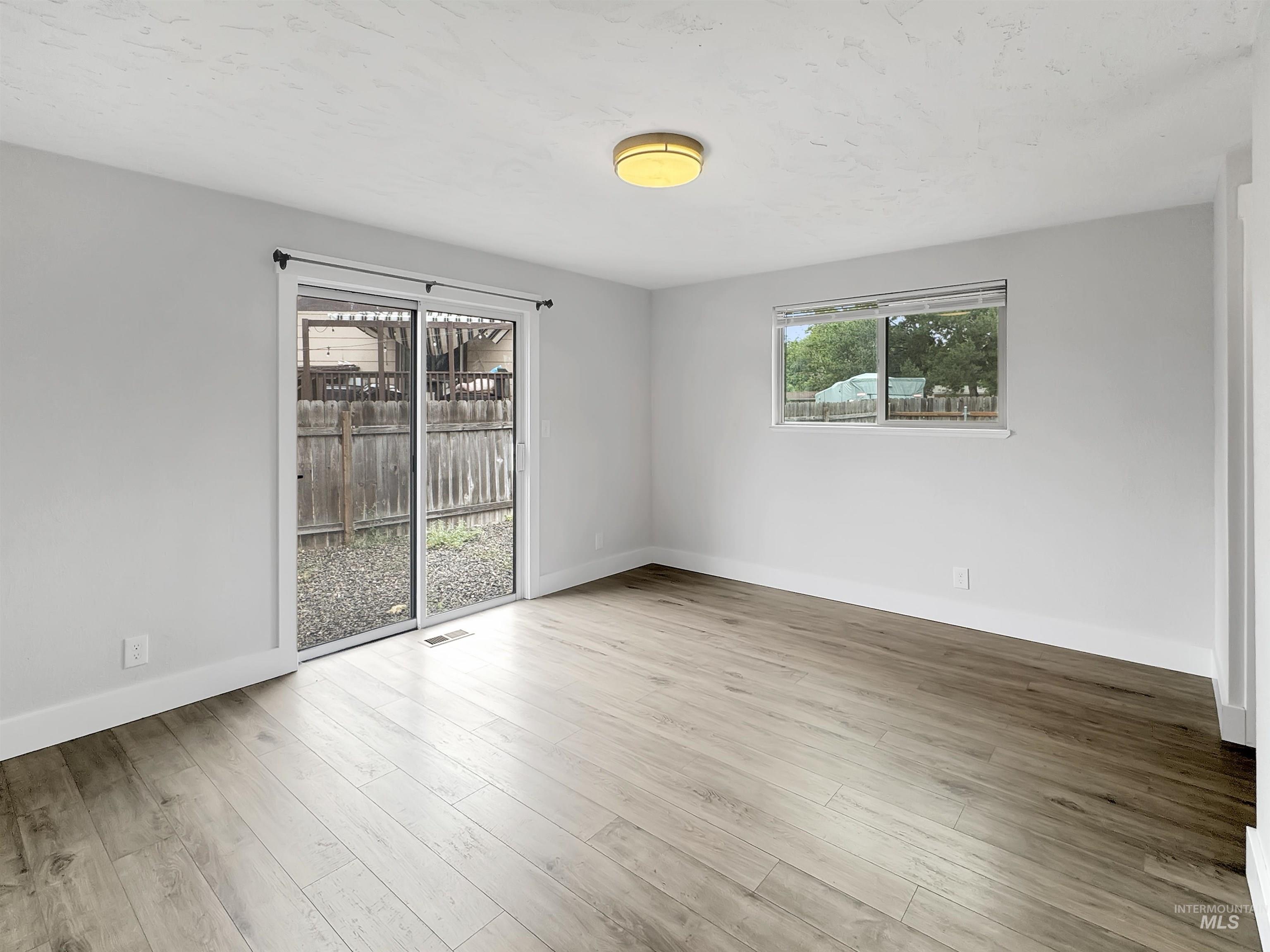 Spacious room featuring light wood-finish flooring, white walls, and a contemporary ceiling light fixture