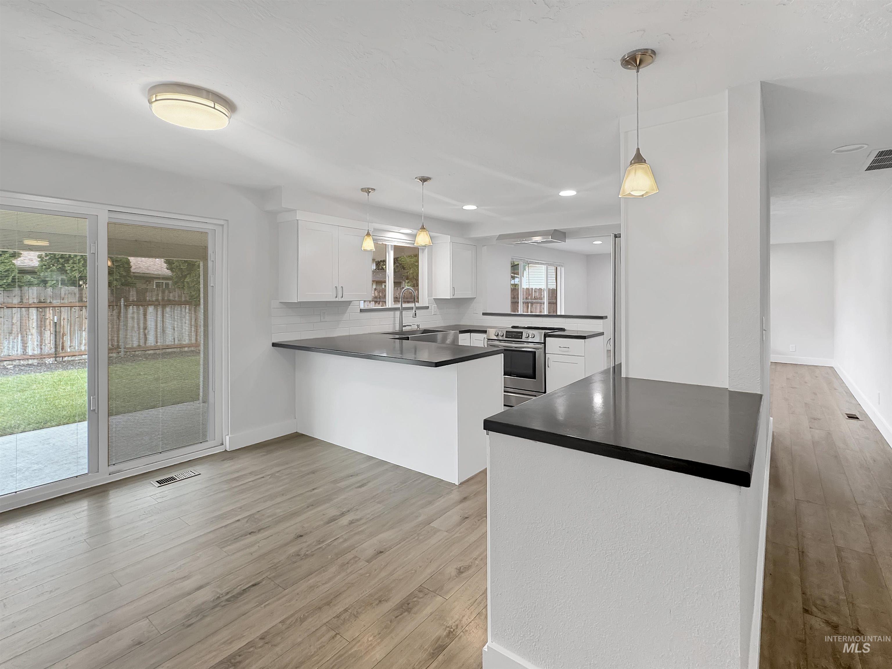 Kitchen and dining area featuring wood-finish flooring, white cabinetry, dark countertops, and stainless steel appliances