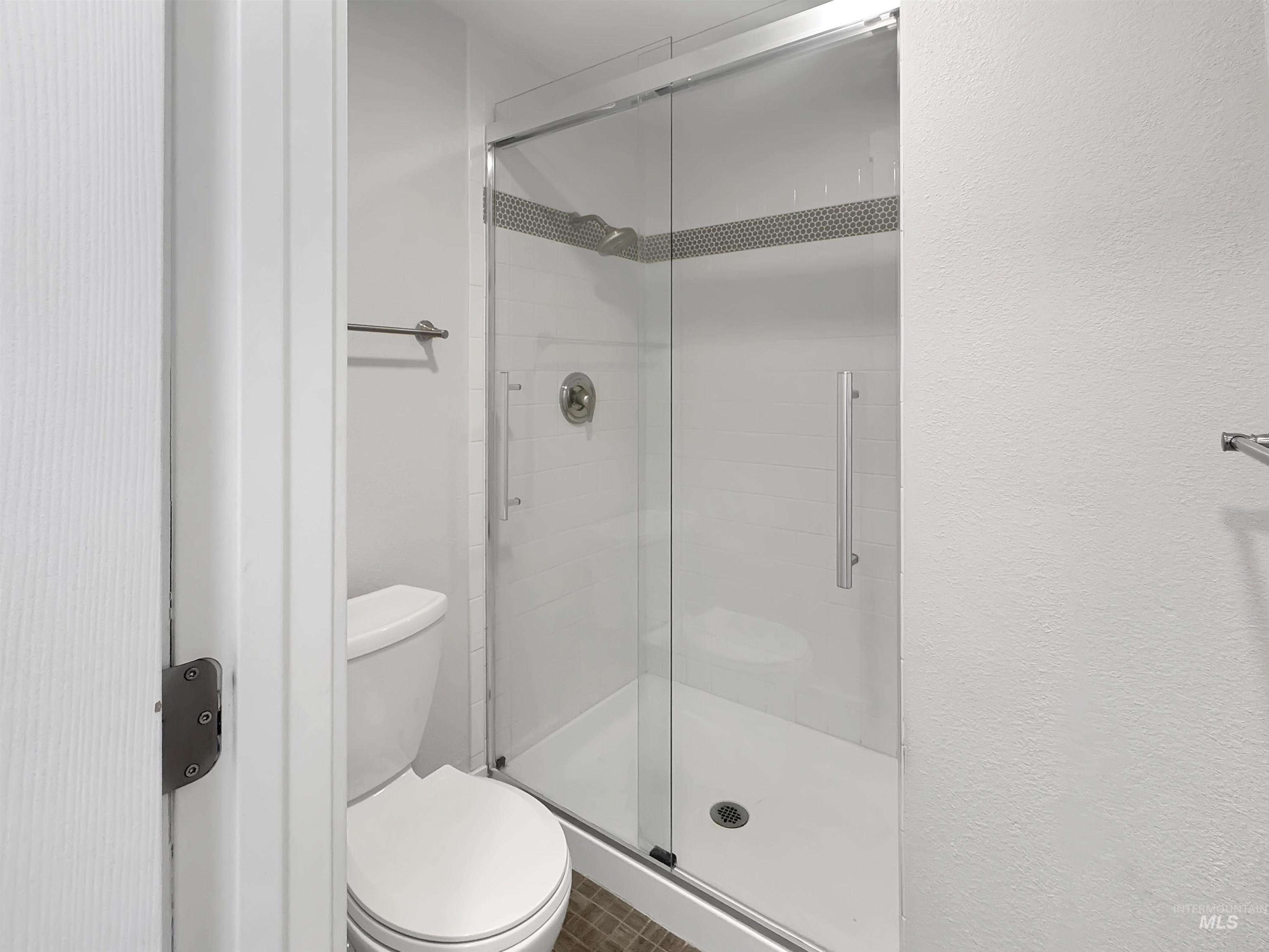 Contemporary bathroom featuring a frameless glass shower enclosure, white subway tile shower surround, chrome fixtures, a modern toilet, and textured wall finishes
