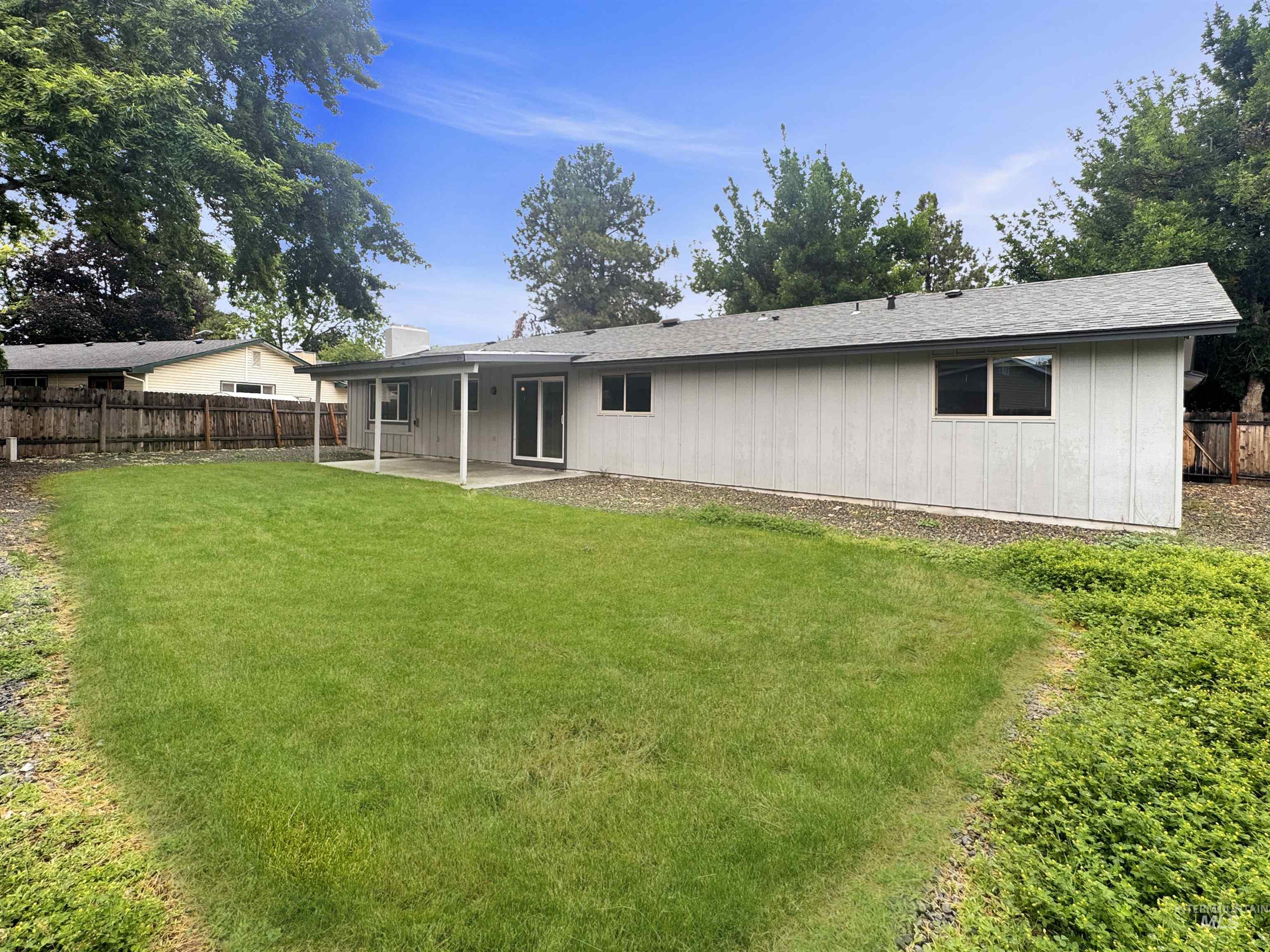 Expansive backyard featuring a manicured lawn, covered patio, and mature perimeter trees