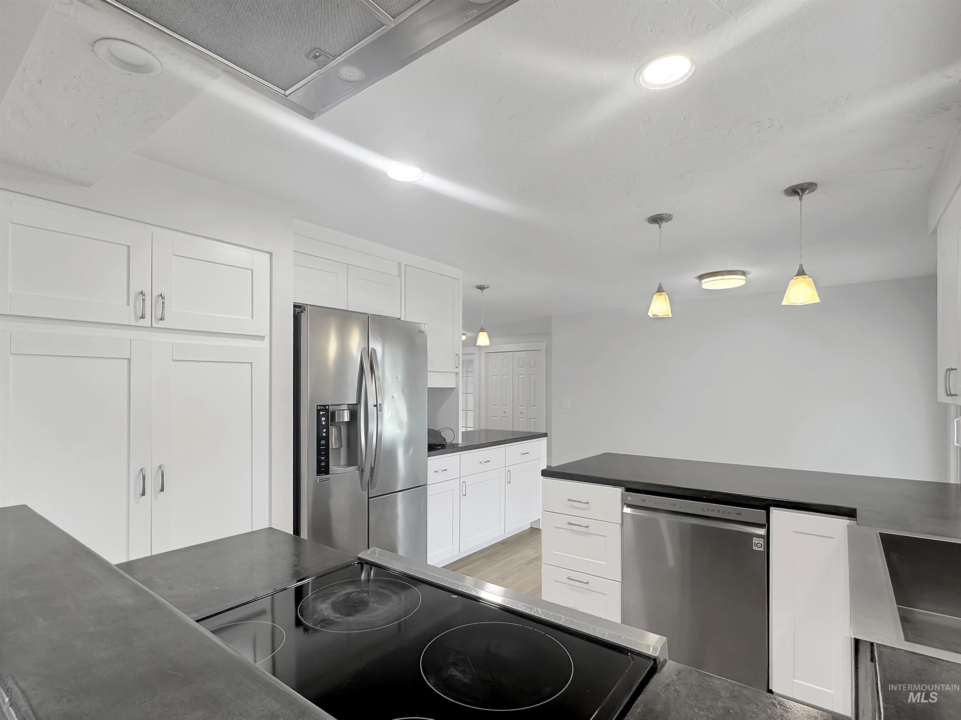Modern kitchen featuring white shaker cabinetry, stainless steel appliances, dark countertops, recessed lighting, and pendant lights