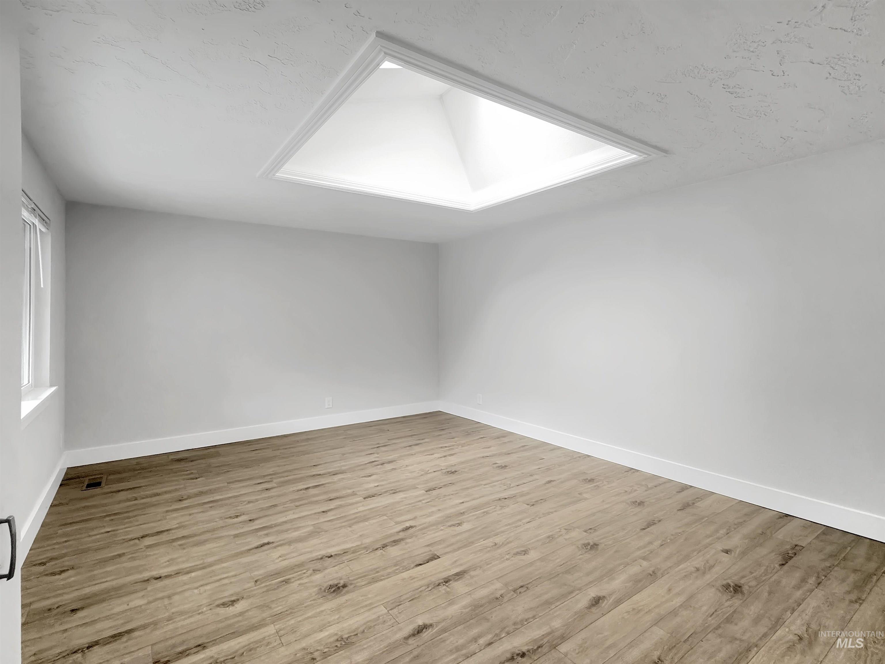 Spacious interior featuring a large ceiling skylight, wood-finish flooring, white baseboards, and a window with white trim