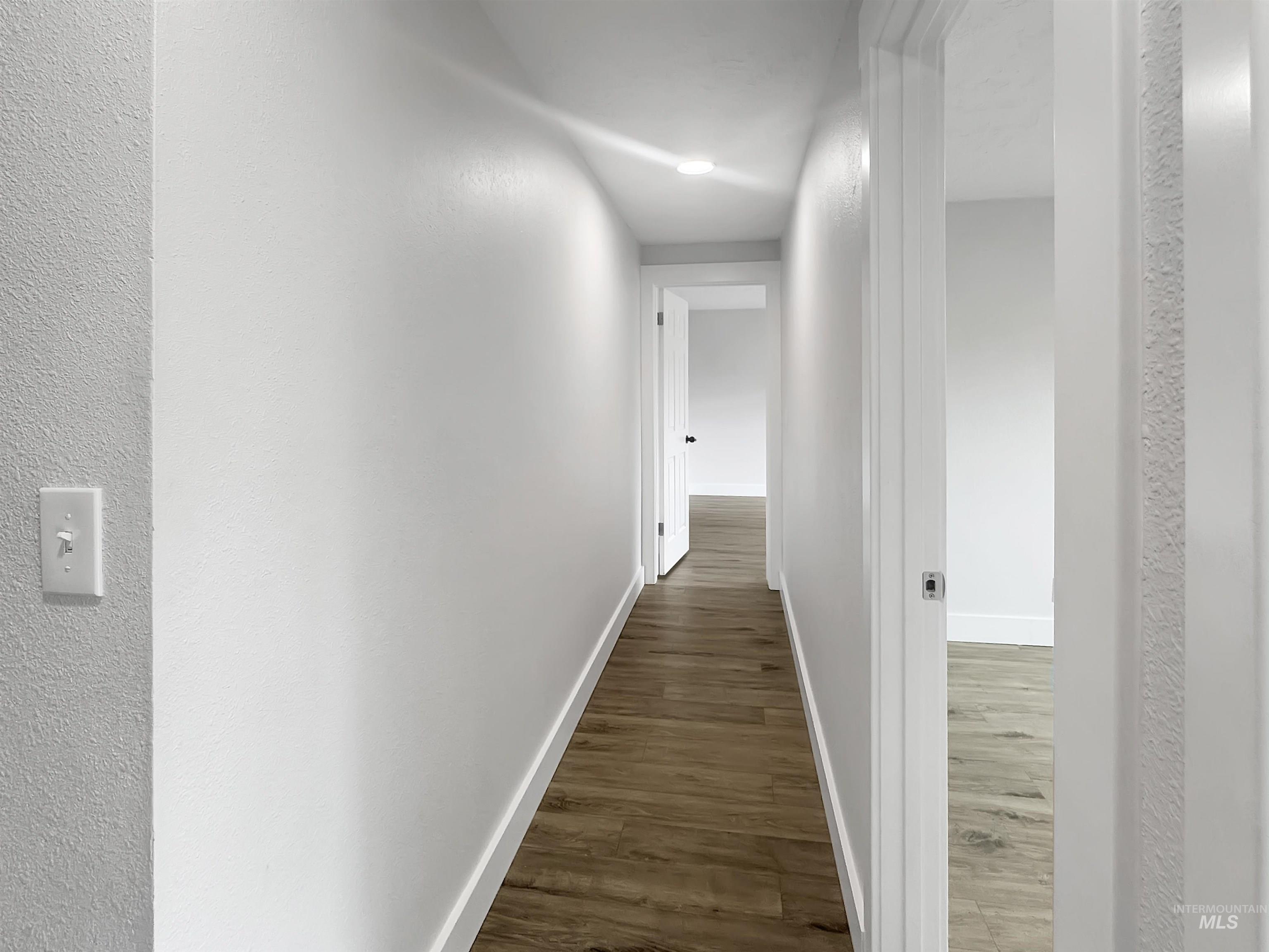 Hallway featuring wood-finish flooring, white baseboards, recessed lighting, and white interior doors