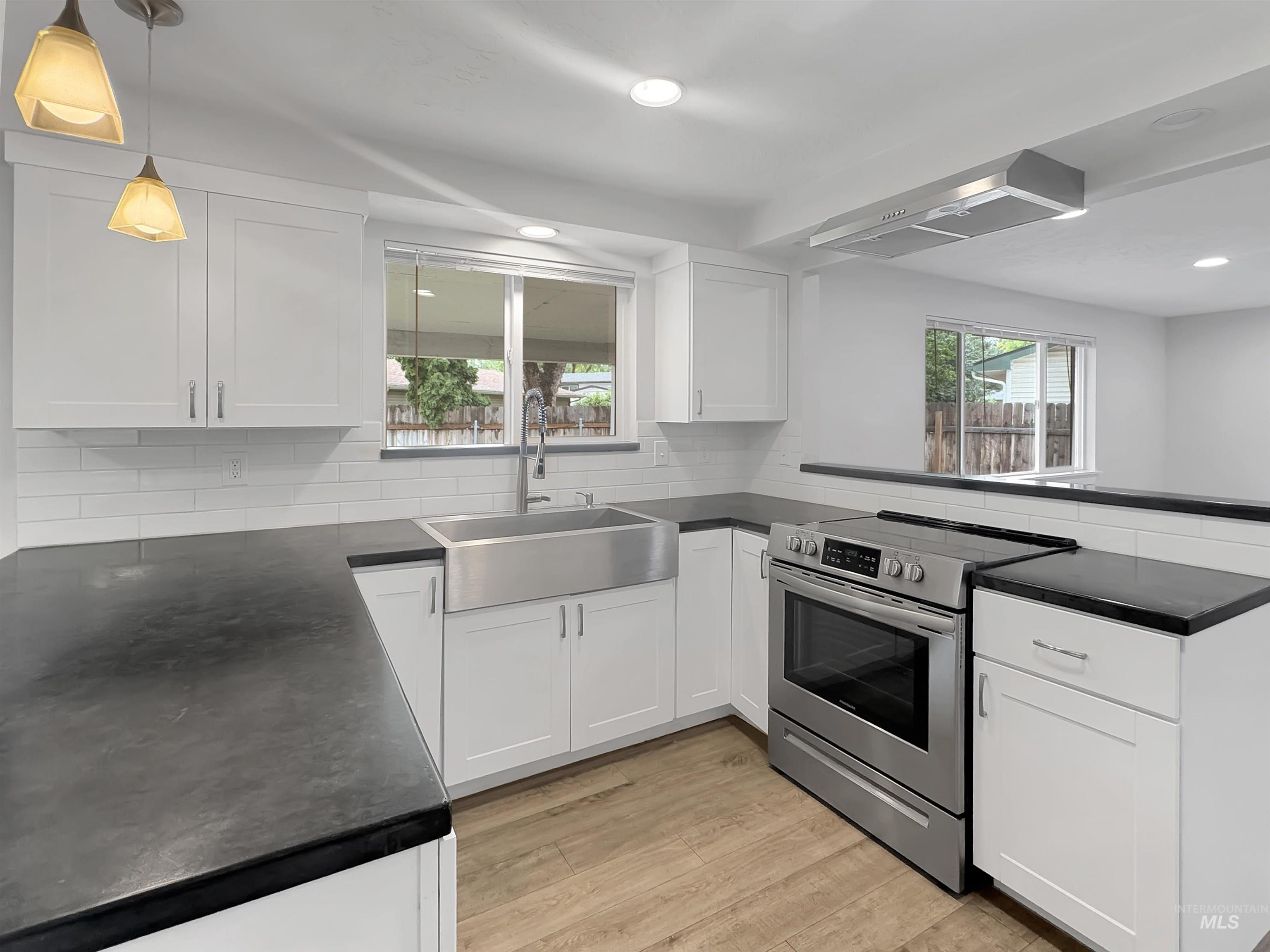 Modern kitchen featuring white shaker-style cabinetry, dark countertops, and stainless steel appliances including a range and farm sink