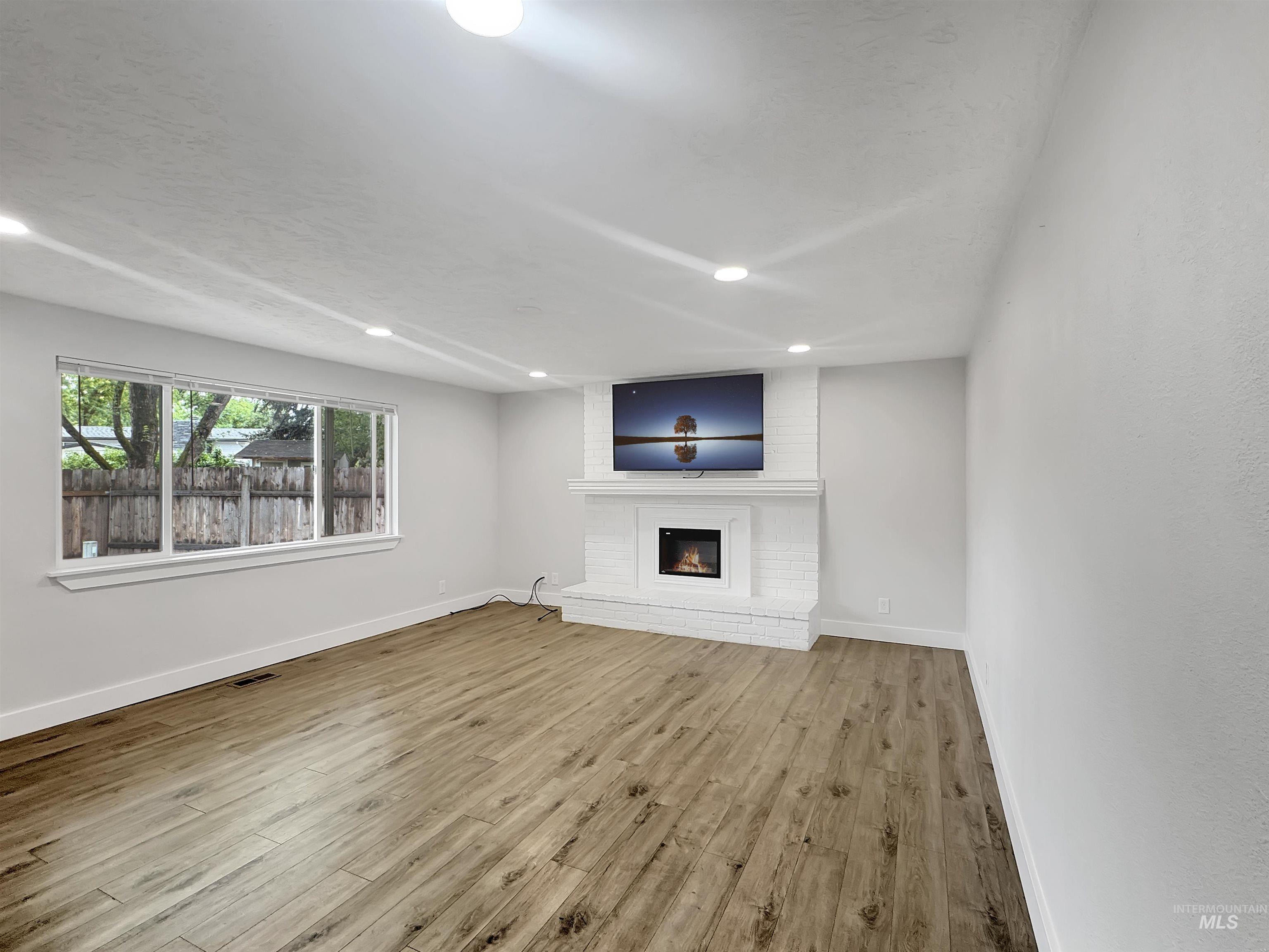 Spacious living area featuring wood-finish flooring, a white brick fireplace with a mantle, and recessed lighting