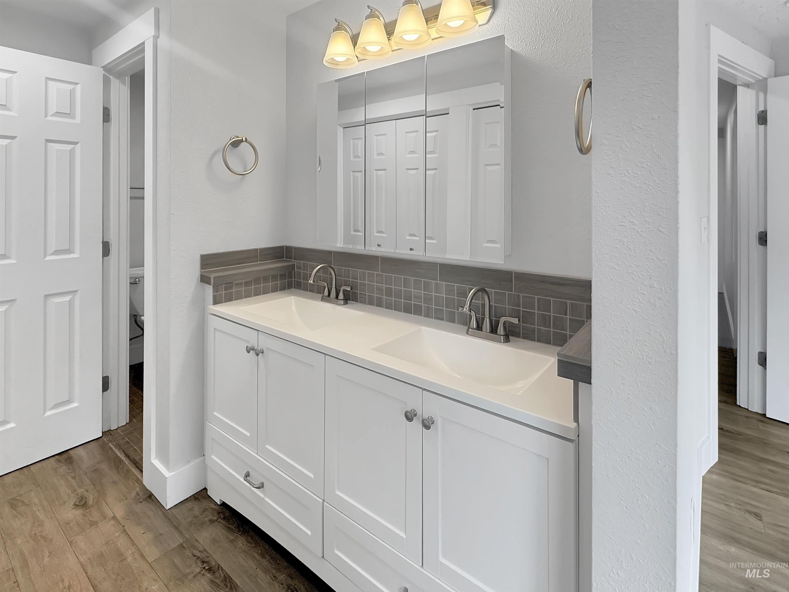 Double vanity with integrated sinks, white cabinetry, chrome fixtures, and a gray mosaic tile backsplash