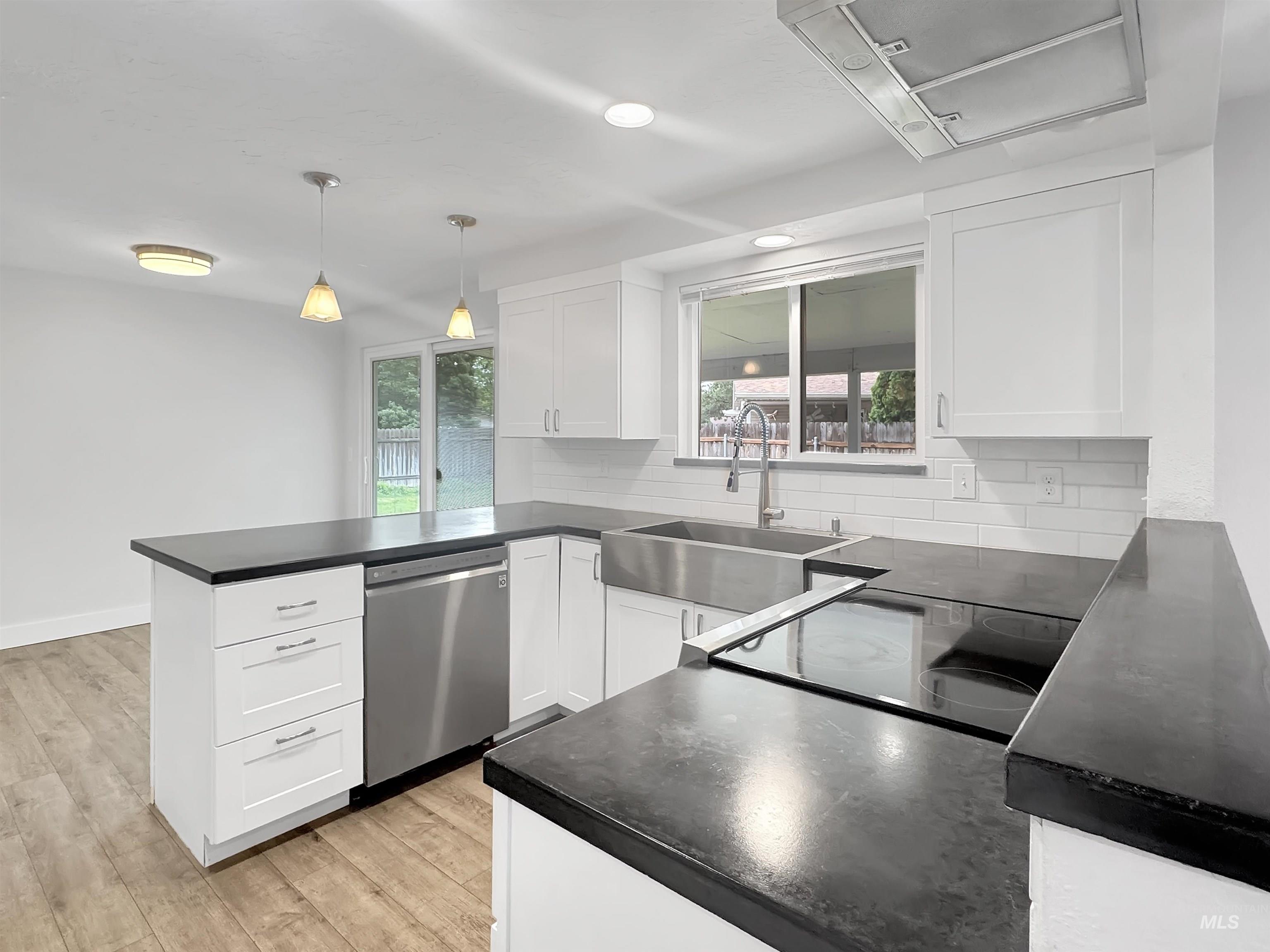 Modern kitchen featuring white shaker cabinetry, dark countertops, a stainless steel farmhouse sink, an integrated cooktop, and wood-finish flooring