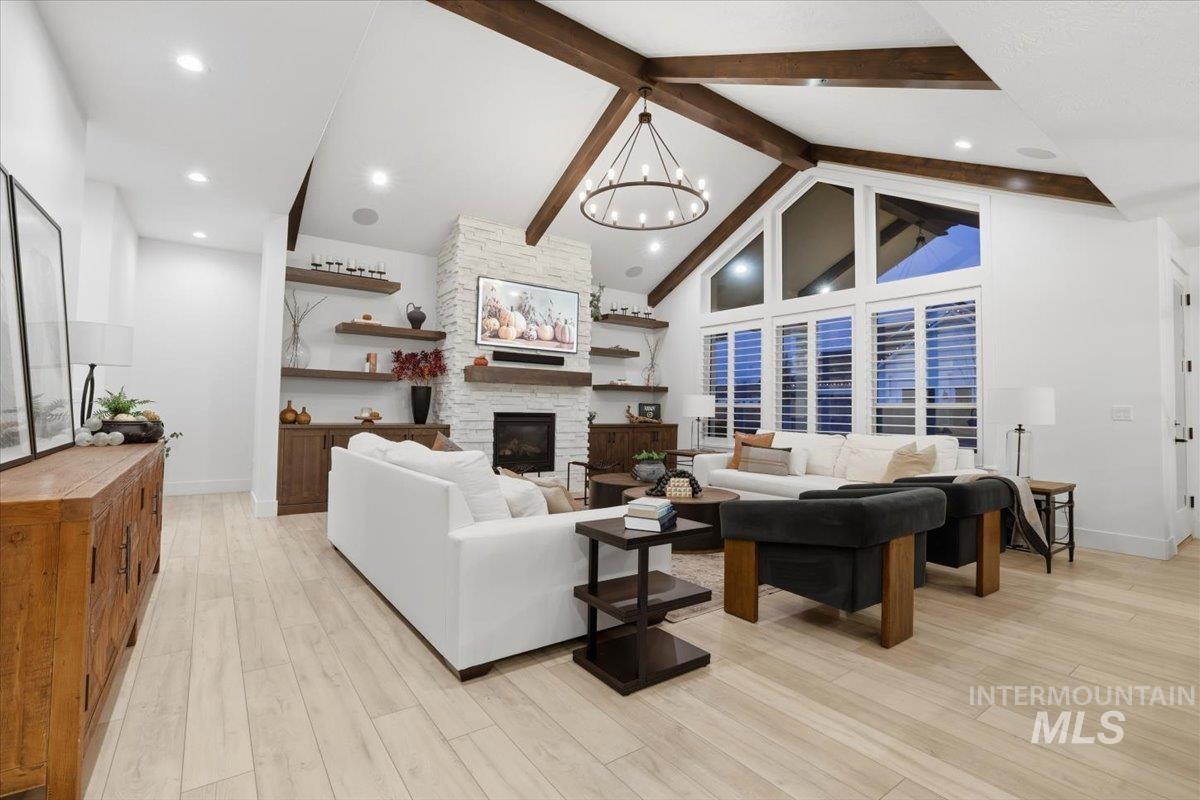 Living area with a fireplace, light wood-style floors, high vaulted ceiling, a chandelier, and recessed lighting