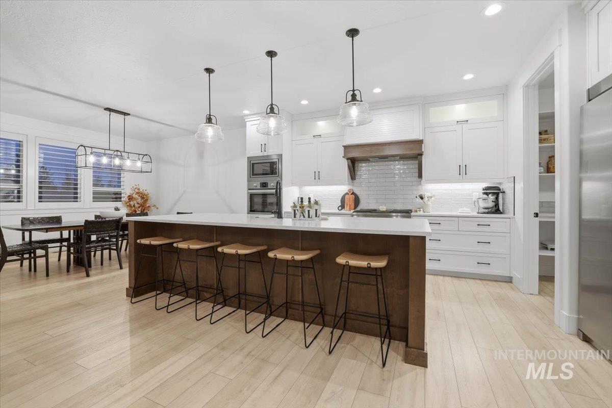 Kitchen with a kitchen breakfast bar, decorative light fixtures, white cabinets, a kitchen island, and backsplash
