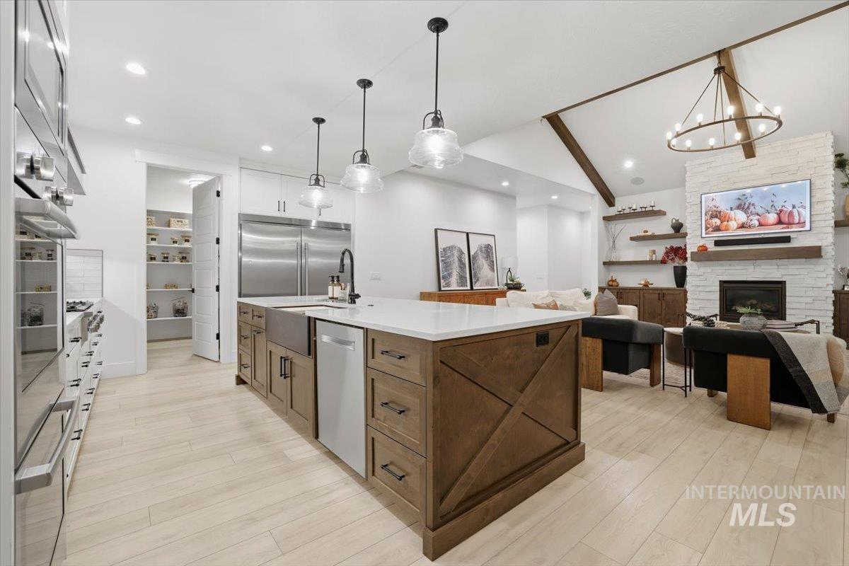 Kitchen featuring open floor plan, decorative light fixtures, an island with sink, light wood-style flooring, and vaulted ceiling