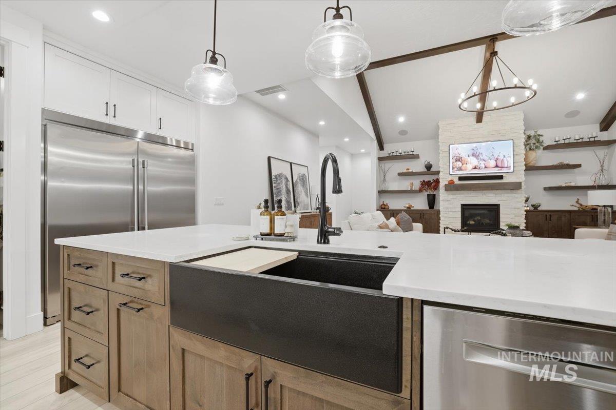 Kitchen with open floor plan, stainless steel appliances, light stone countertops, decorative light fixtures, and a fireplace