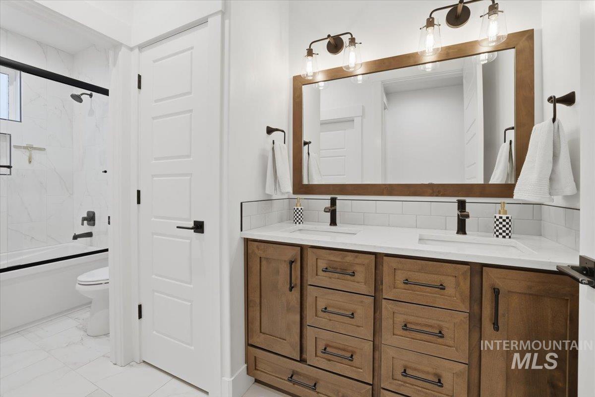 Bathroom with double vanity, combined bath / shower with glass door, light marble finish floors, and backsplash