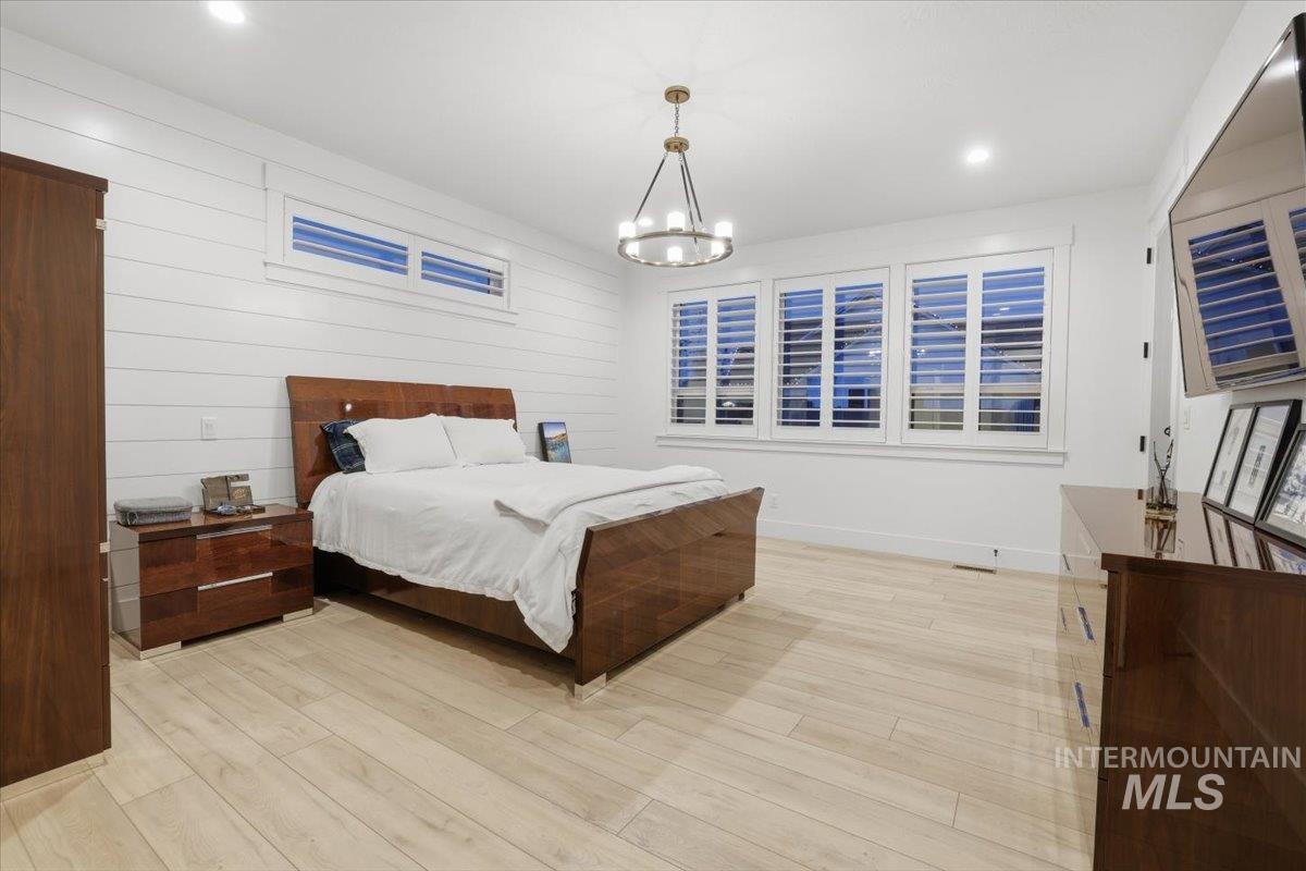 Bedroom with light wood-type flooring, recessed lighting, a chandelier, and wooden walls